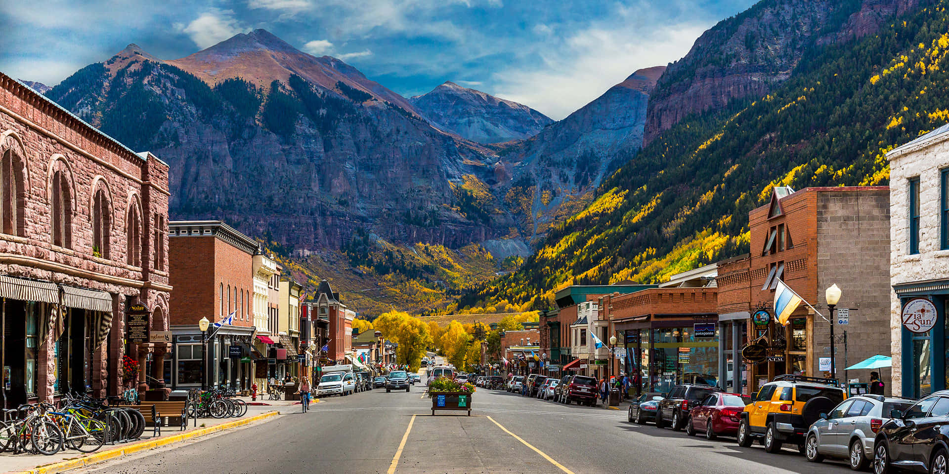 Colorado Mountain 桌布 壁紙 — 一條充滿活力的山城街道，兩旁是磚砌建築和秋樹，上方是明亮的藍天。