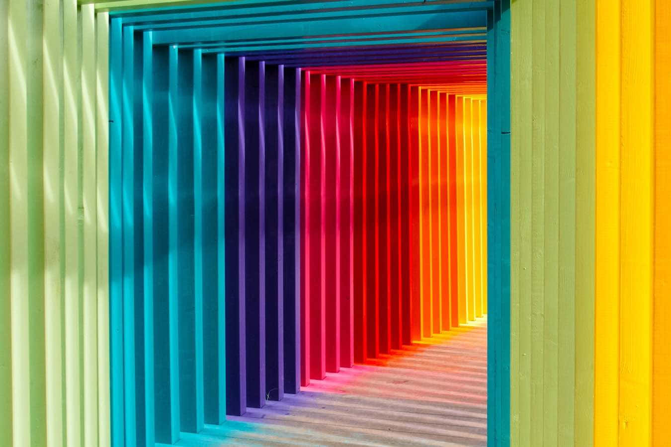 Color Palette 桌布 壁紙 — 一條充滿活力的彩虹色走廊，帶有波浪狀的垂直面板，營造出引人入勝的視覺錯覺，通向遠方。