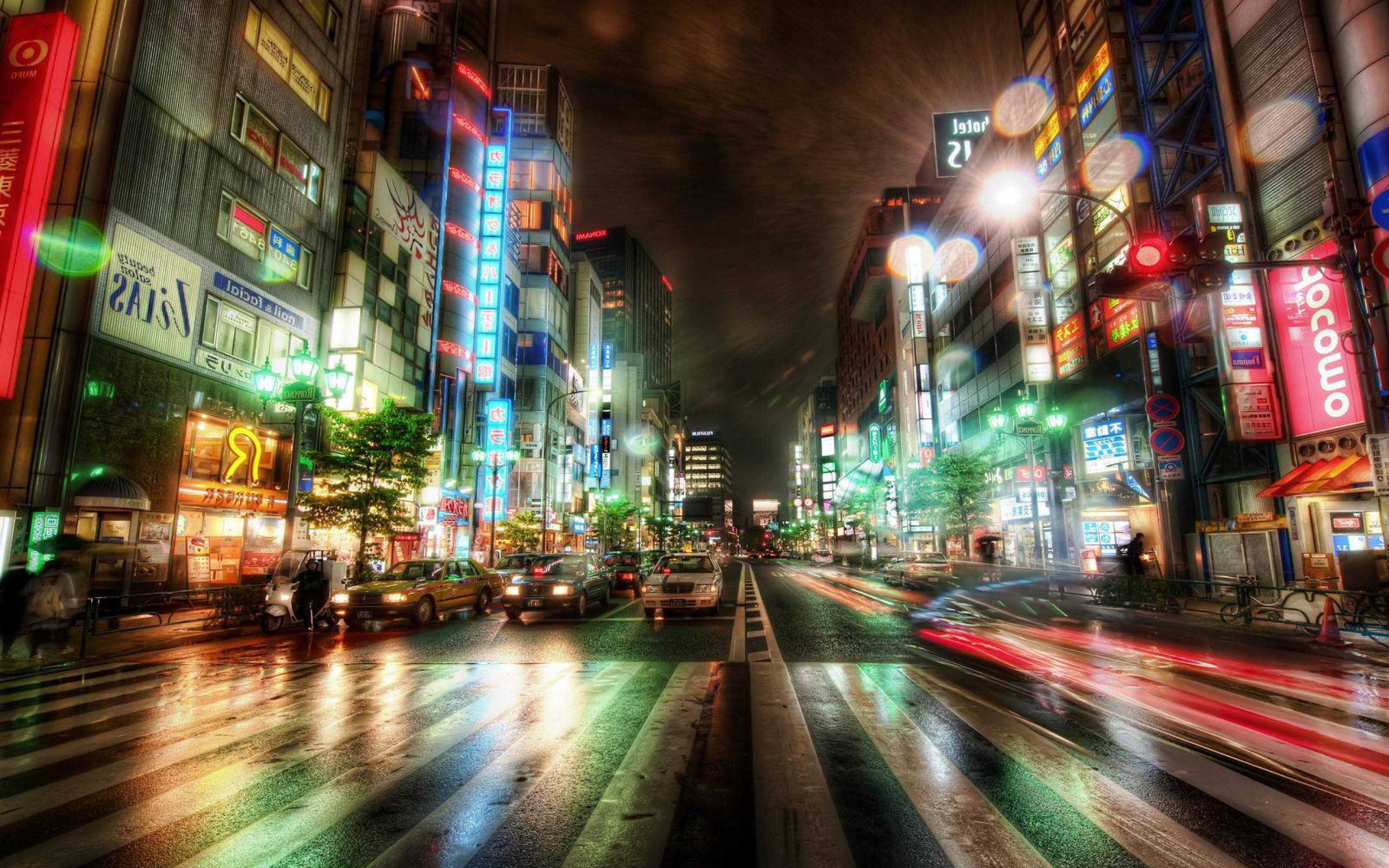 漂亮的桌面 桌布 壁紙 — 一條充滿活力的東京霓虹燈街道夜景，濕漉漉的路面反射出五彩繽紛的燈光和汽車拖曳的光跡。