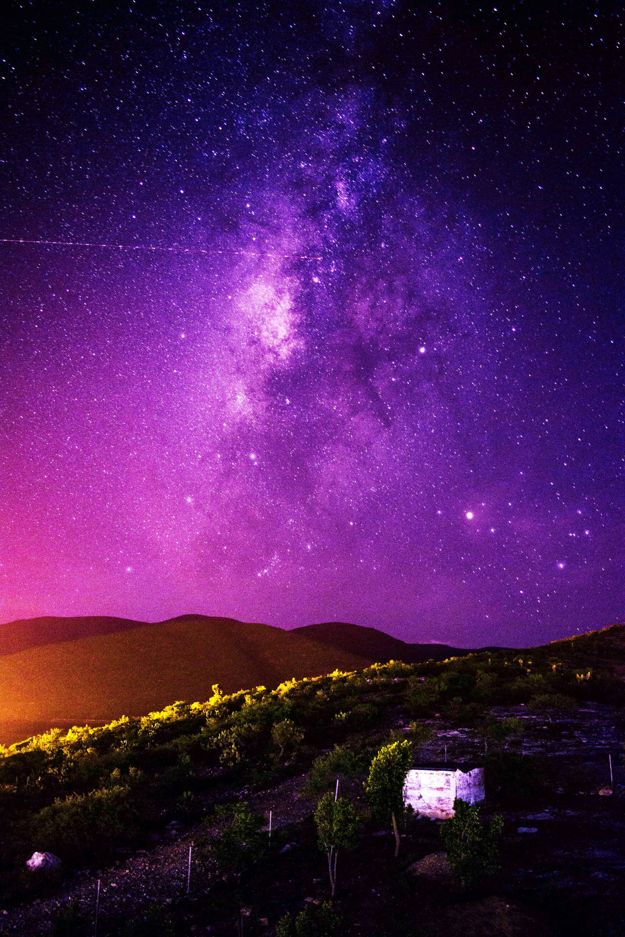 在充滿活力的紫色星空下，背景是山丘，一個發光的石結構。 — 4K 壁紙