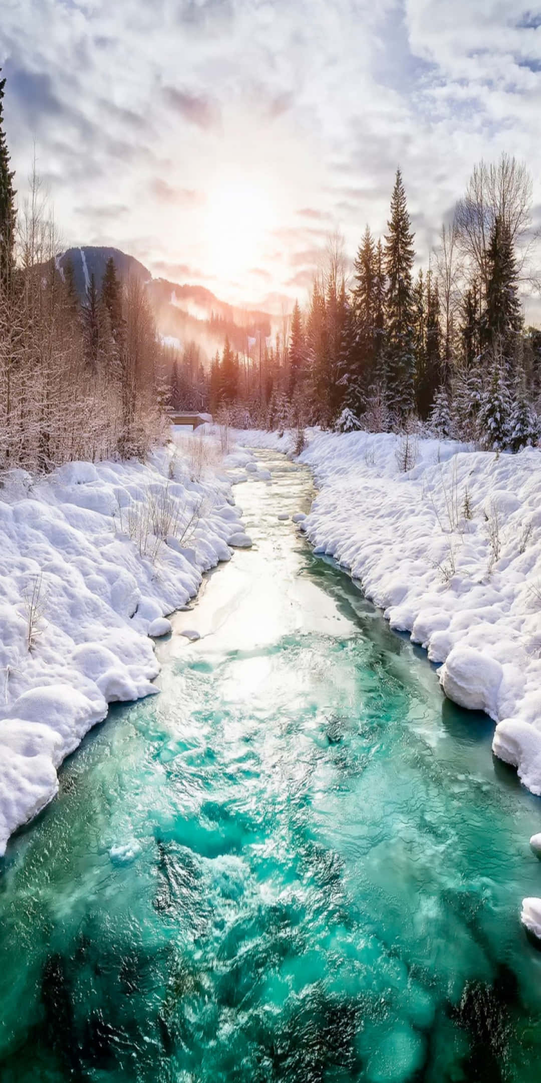 自然 桌布 壁紙 — 一條充滿活力的藍綠色河流流經白雪覆蓋的冬季森林，上方有陽光照射的雲朵。