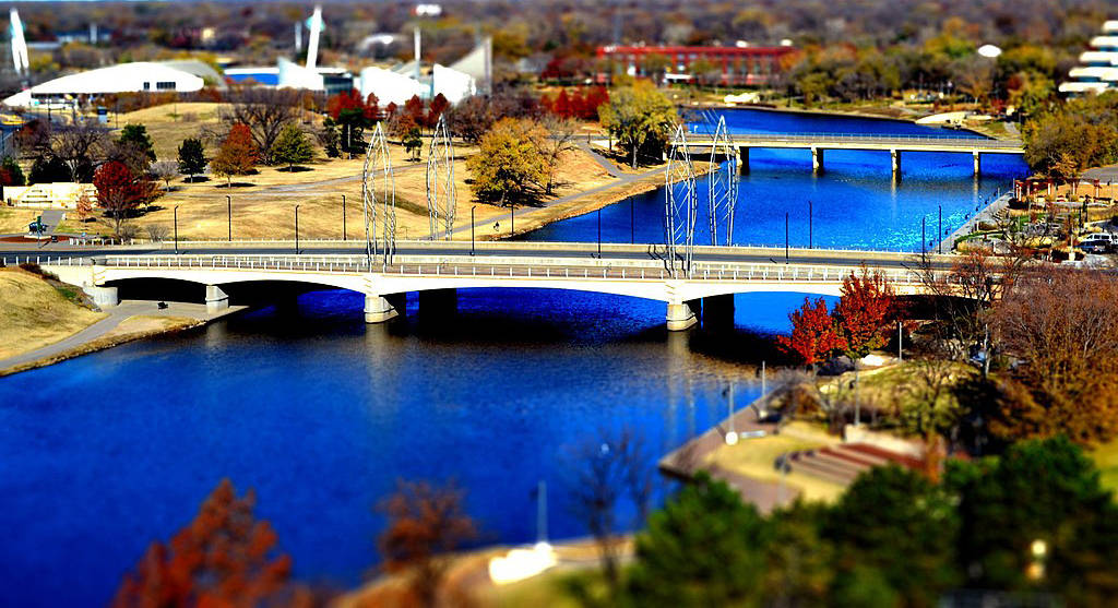 風景 桌布 壁紙 — 一條充滿活力的藍色河流在現代橋樑下流淌，周圍環繞著秋樹和城市建築。