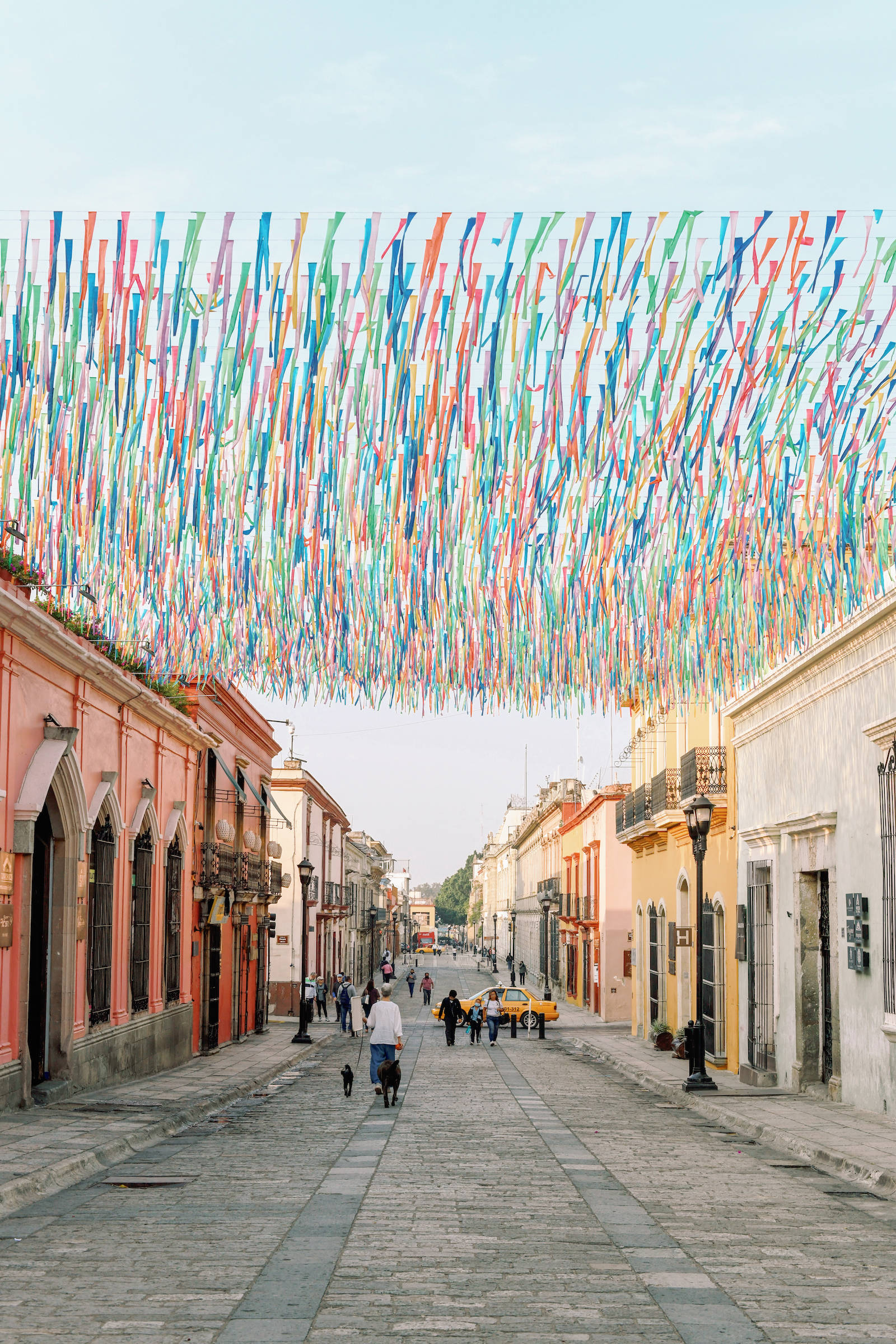 Mexican 桌布 壁紙 — 一條充滿活力的街道，兩旁是色彩繽紛的殖民時期建築，頭頂上是耀眼的多色絲帶天篷。