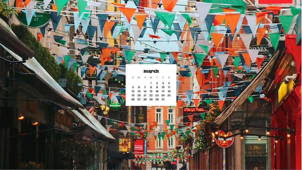 March Desktop 桌布 壁紙 — 一條充滿活力的街道，掛滿橙色、綠色和白色的三角形旗幟，在明亮的天空下，並有日曆疊加。