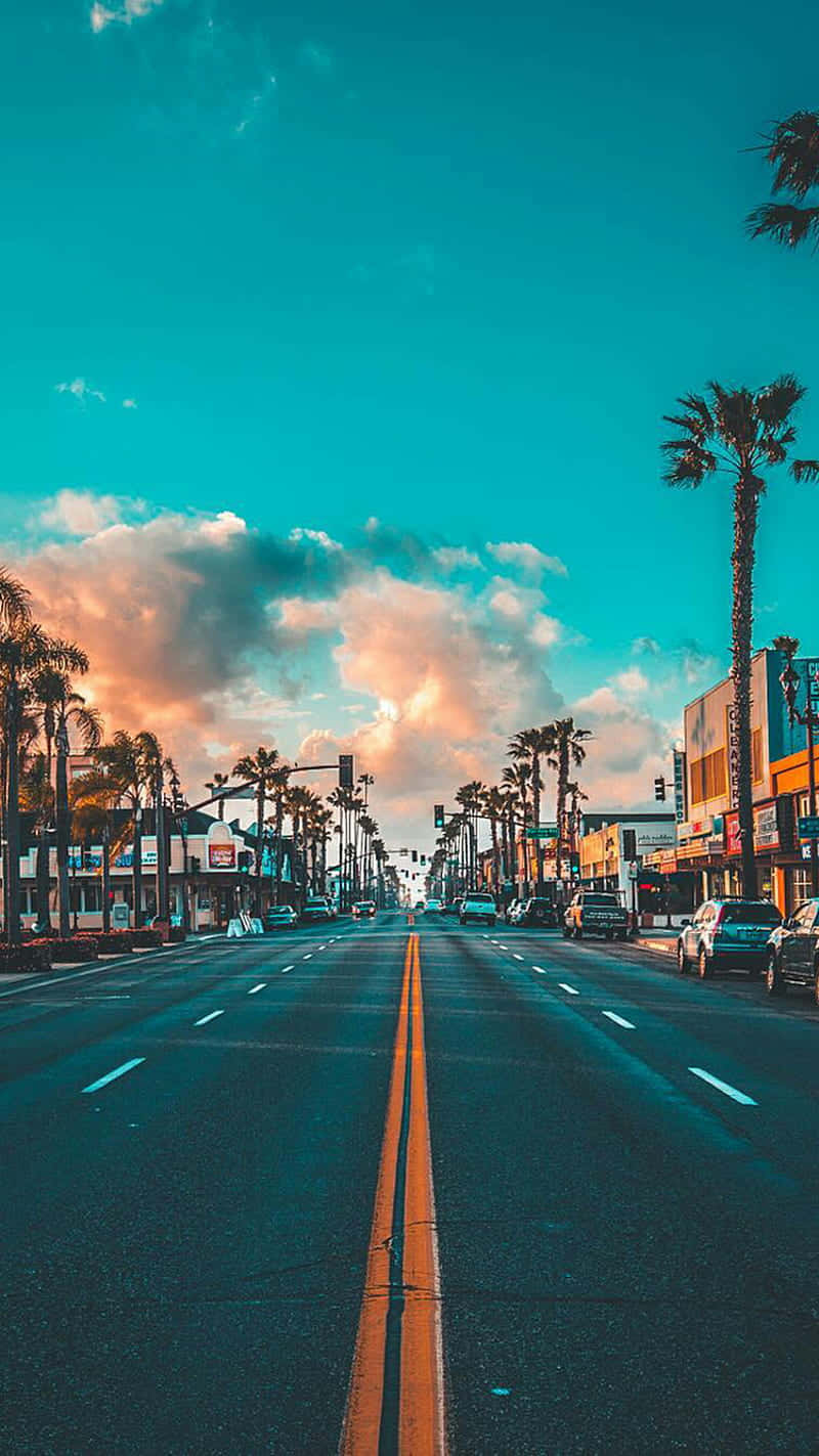 Pixel 3 California 桌布 壁紙 — 一條充滿活力的街道兩旁種滿棕櫚樹，延伸向色彩繽紛的日落天空，天空中有蓬鬆的雲朵。