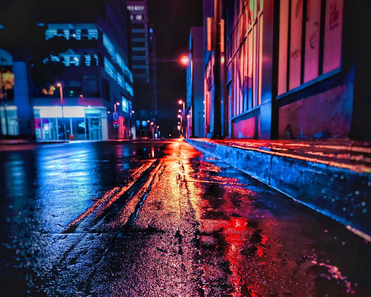 standard 桌布 壁紙 — 一條充滿霓虹燈的都市街道在夜晚將鮮豔的紅藍燈光反射在濕漉漉的路面上，周圍是高聳的建築物。