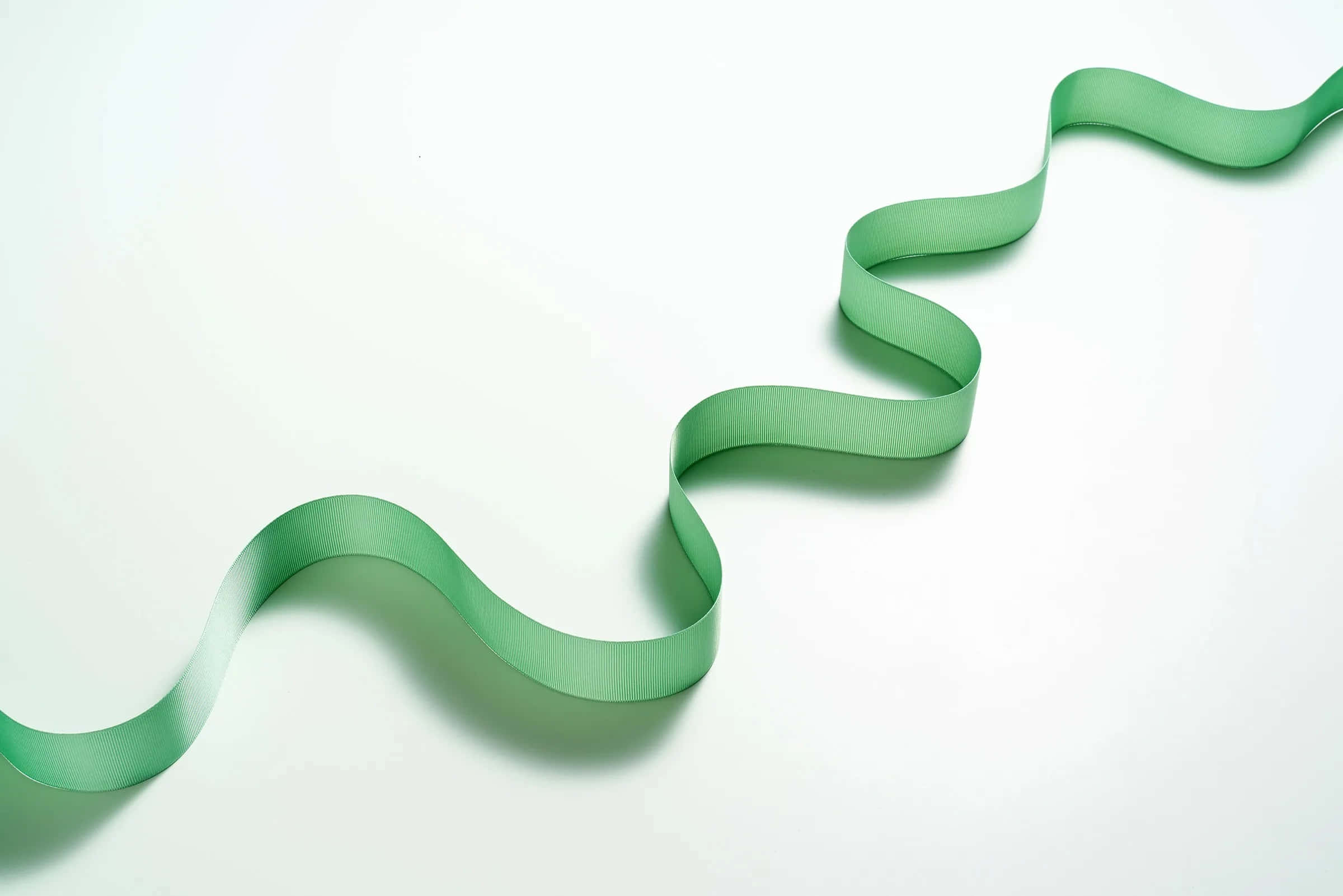 ribbon 桌布 壁紙 — 一條光滑的淺綠色絲帶優雅地彎曲在明亮的白色表面上，投下柔和的陰影。