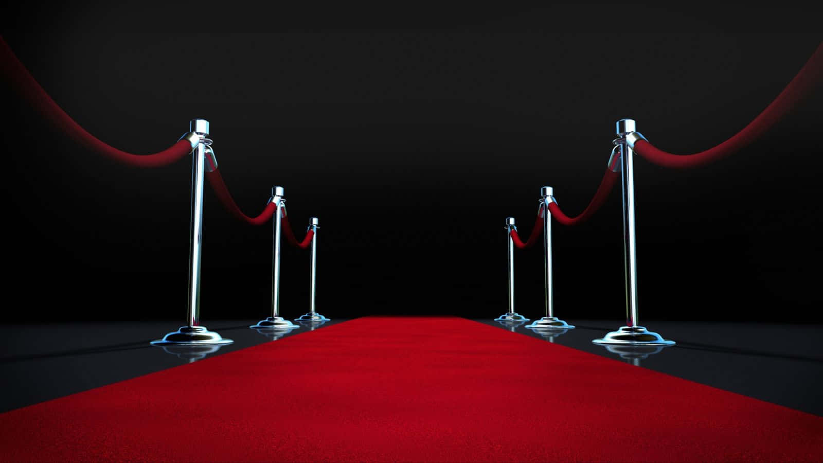 Red Carpet 桌布 壁紙 — 一條光滑的紅色地毯在戲劇性的聚光燈下延伸進黑暗，兩側是銀色立柱和天鵝絨繩索。