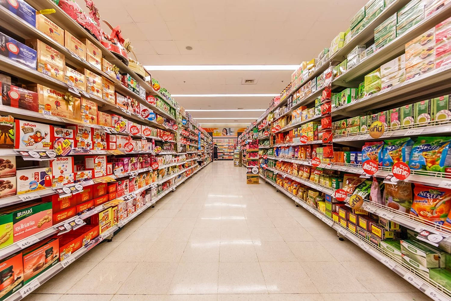 Shopping 桌布 壁紙 — 一條光線充足的超市通道，擺滿了色彩繽紛的零食盒和穀物包裝，一直延伸到遠方。