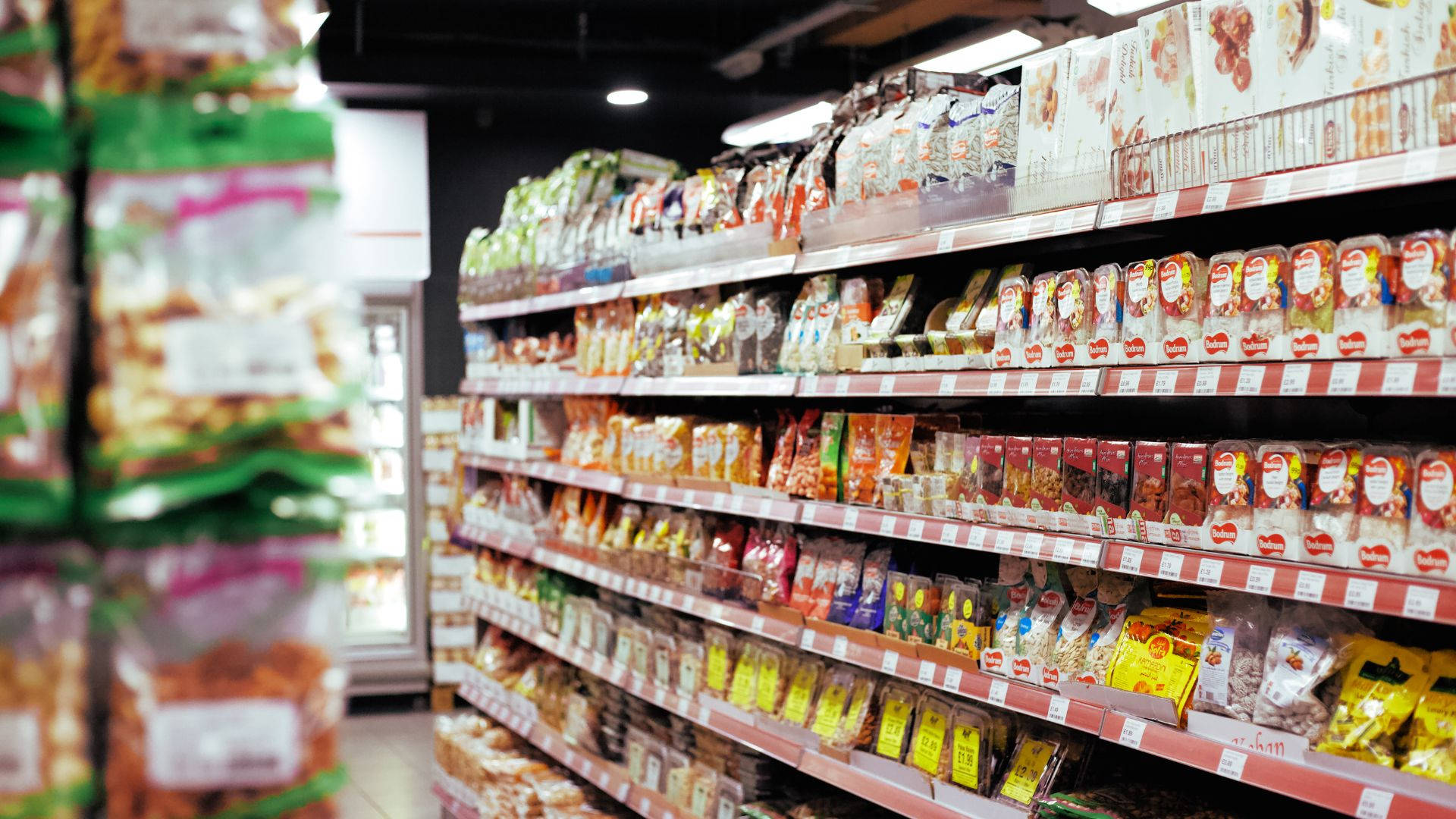 Store 桌布 壁紙 — 一條光線充足的雜貨店通道，整齊的貨架上擺滿了色彩繽紛的零食包裝。