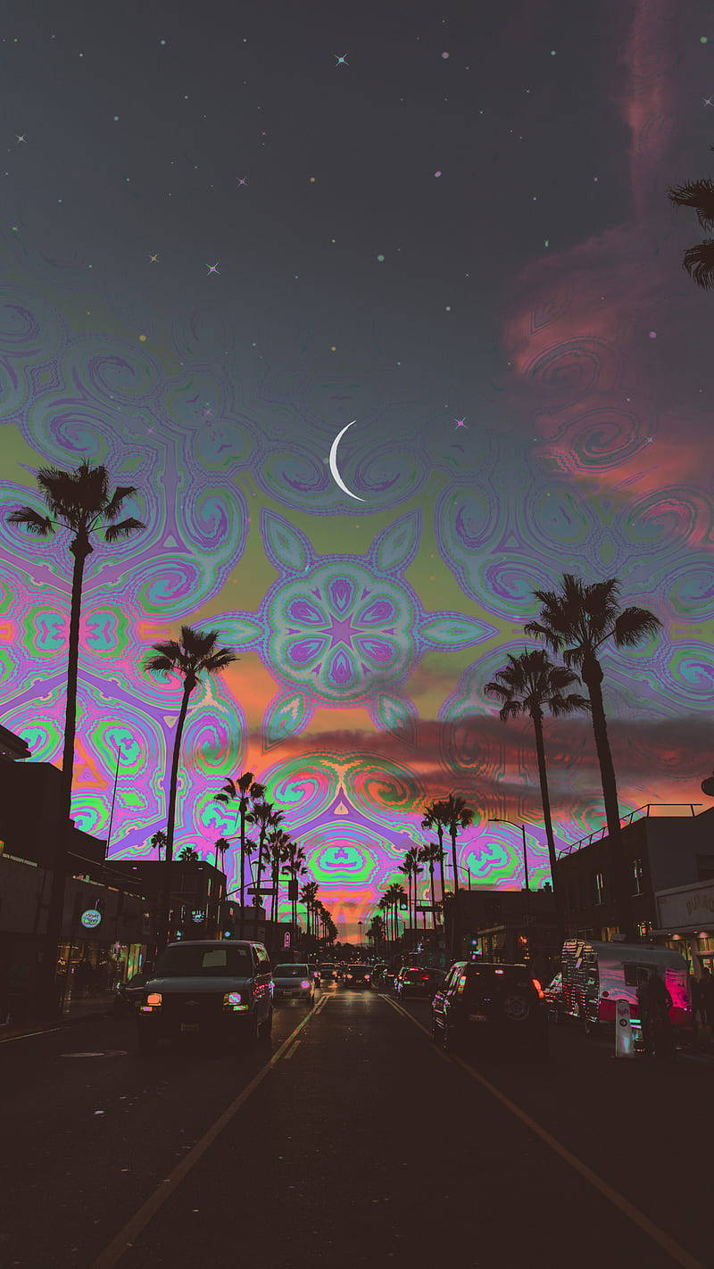 Trippy Dope 桌布 壁紙 — 一條兩旁種滿棕櫚樹的街道，上方是超現實的夜空，充滿發光的迷幻圖案和一彎新月。