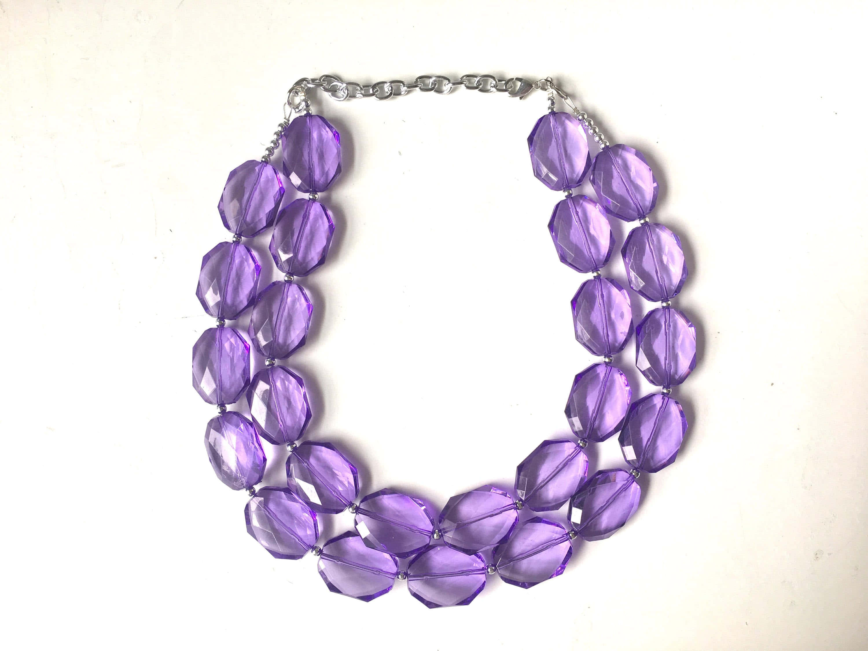 Purple Jewelry 桌布 壁紙 — 一條分層項鍊，帶有刻面紫色珠子和銀鏈，放在純白色表面上。