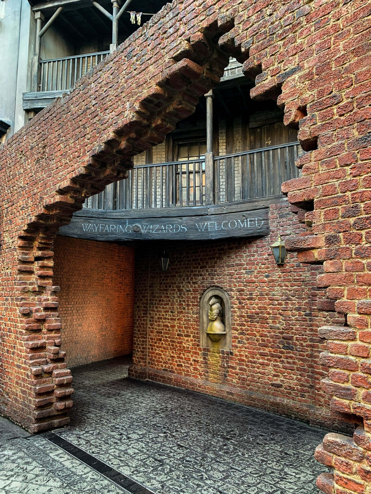 Diagon Alley 桌布 壁紙 — 一條古樸的磚砌拱門，上面有一塊木牌寫著「WAYFARING WIZARDS WELCOMED」，下方是鵝卵石通道。