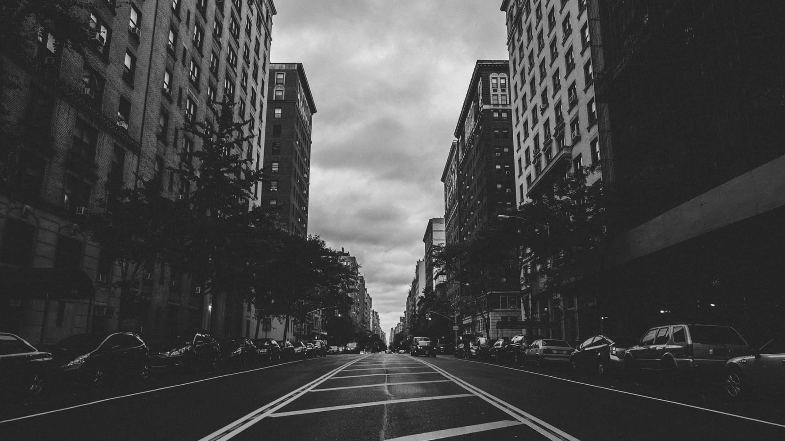 黑白 桌布 壁紙 — 一條單色城市街道，兩旁高樓林立，天空多雲，兩側停滿汽車。