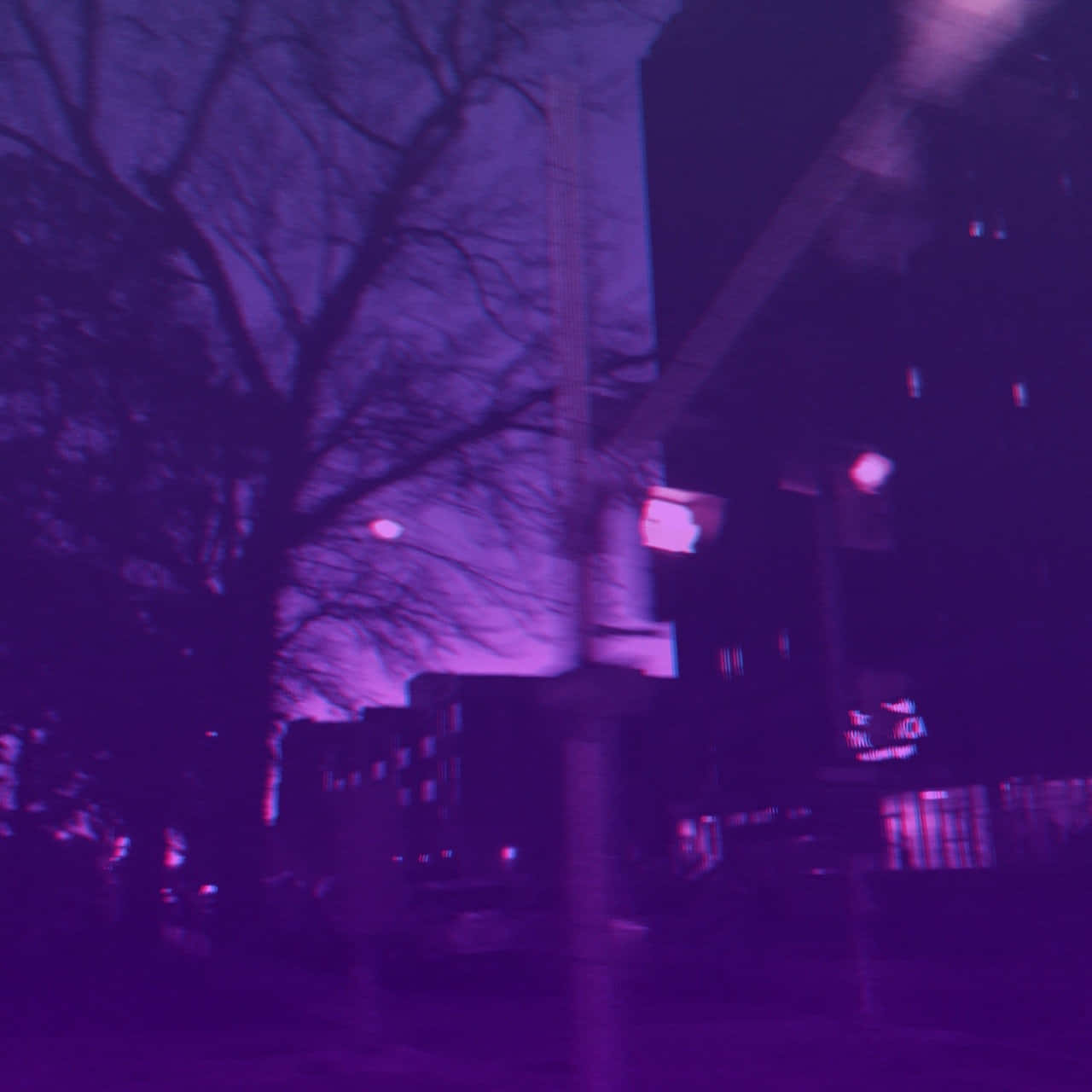 夜景城市 桌布 壁紙 — 一條夜間動態模糊的城市街道，沐浴在強烈的紫色光線中，光禿的樹枝在發光的建築物襯托下形成剪影。