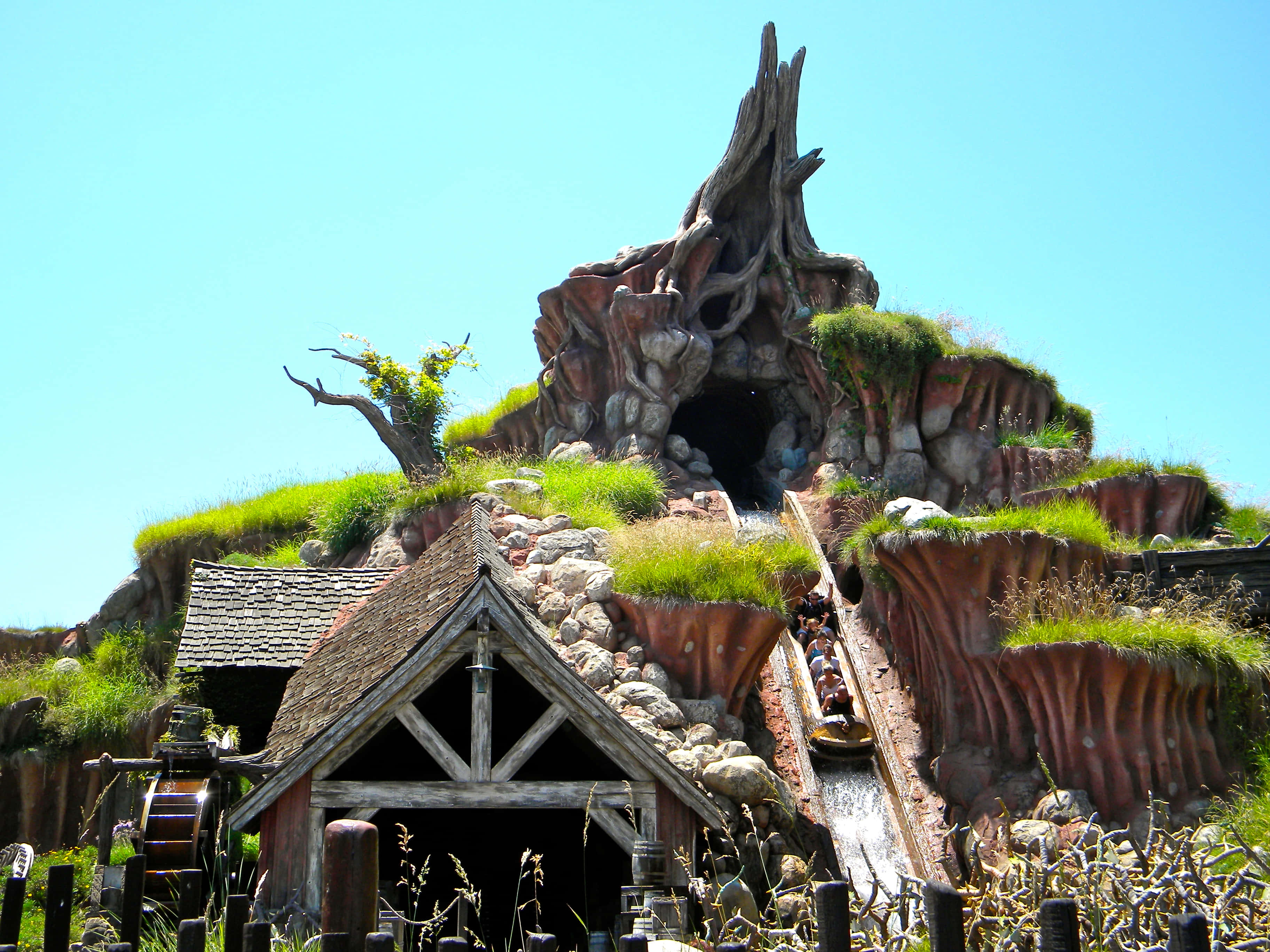 Splash Mountain 桌布 壁紙 — 一條奇特的木製雲霄飛車蜿蜒穿過長滿苔蘚、樹根盤繞的山脈，在清澈的藍天下。