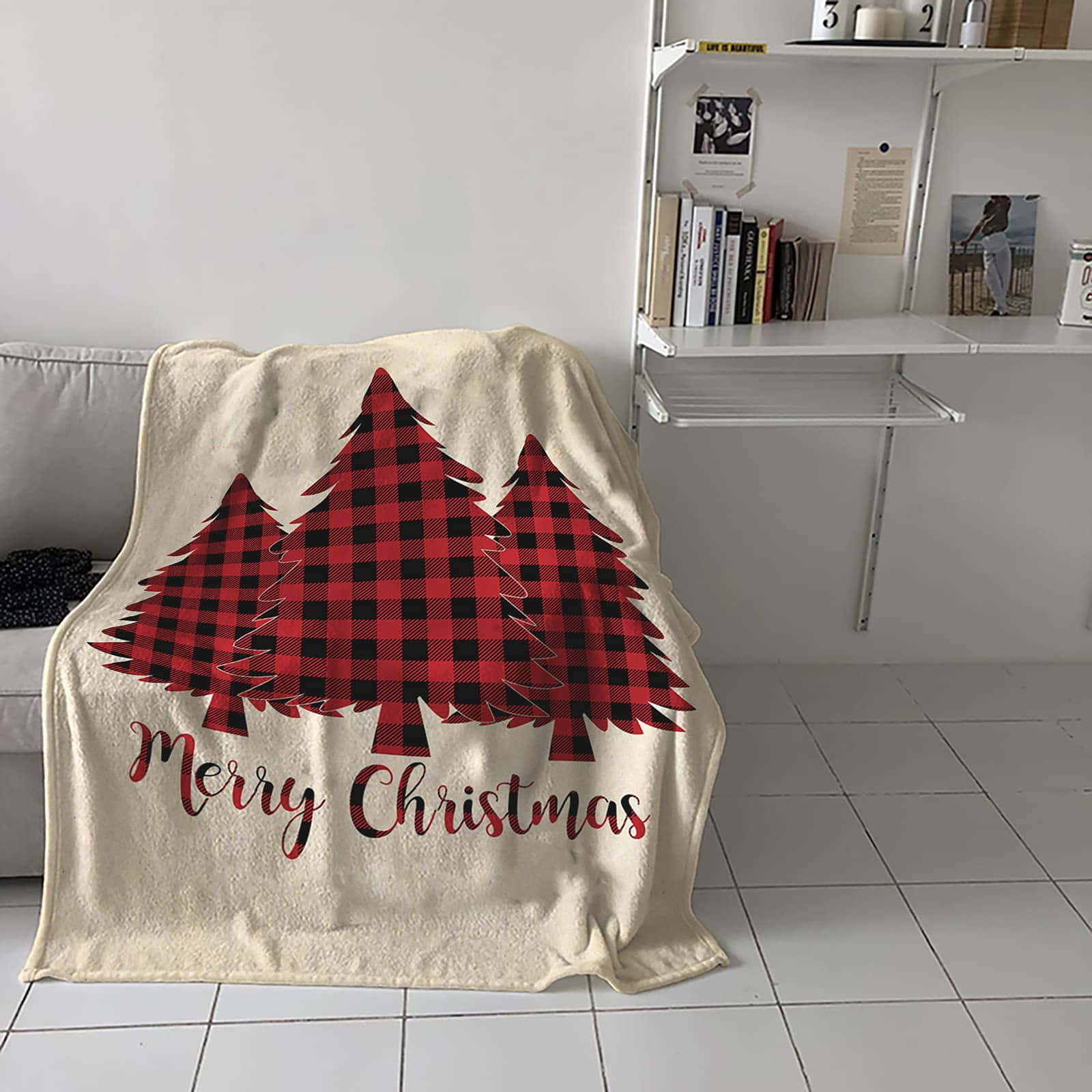 聖誕節 桌布 壁紙 — 一條奶油色毛毯，上面有紅黑格紋松樹和「Merry Christmas」字樣，披在白色瓷磚地板上，靠近沙發和架子。