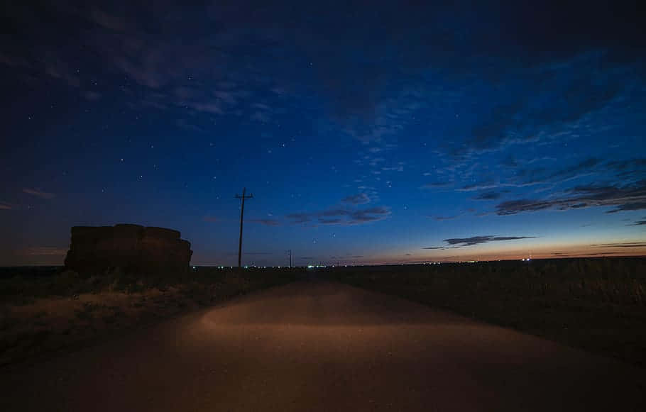 夜空 桌布 壁紙 — 一條孤獨的泥土路在繁星點點的暮色天空下延伸，地平線上有遠處的城市燈光。