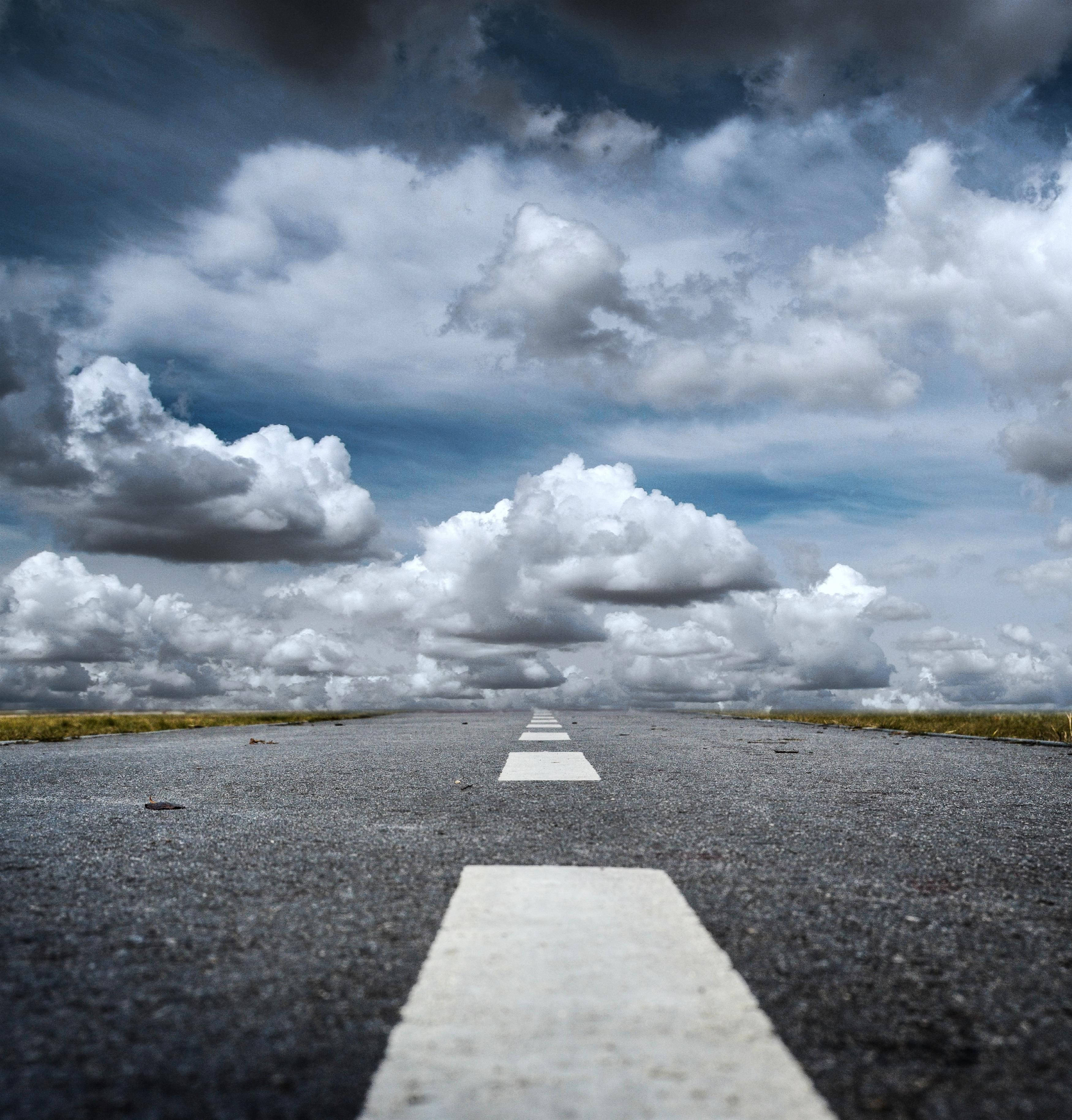 Road 桌布 壁紙 — 一條孤獨的瀝青路延伸向充滿高聳白色和灰色雲朵的戲劇性天空。
