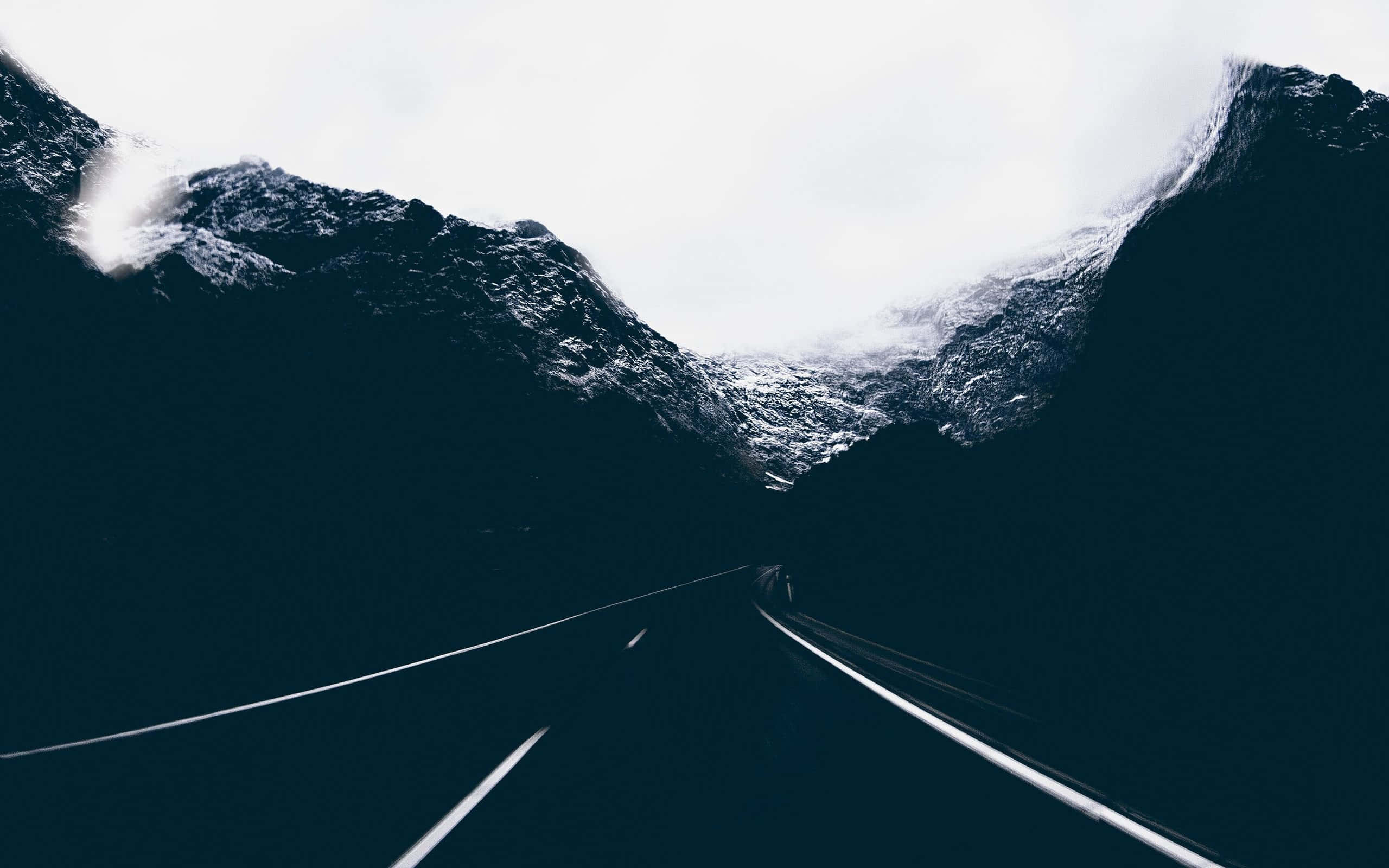 Dark Road 桌布 壁紙 — 一條孤獨的道路蜿蜒穿過高聳的雪山，天空多雲。