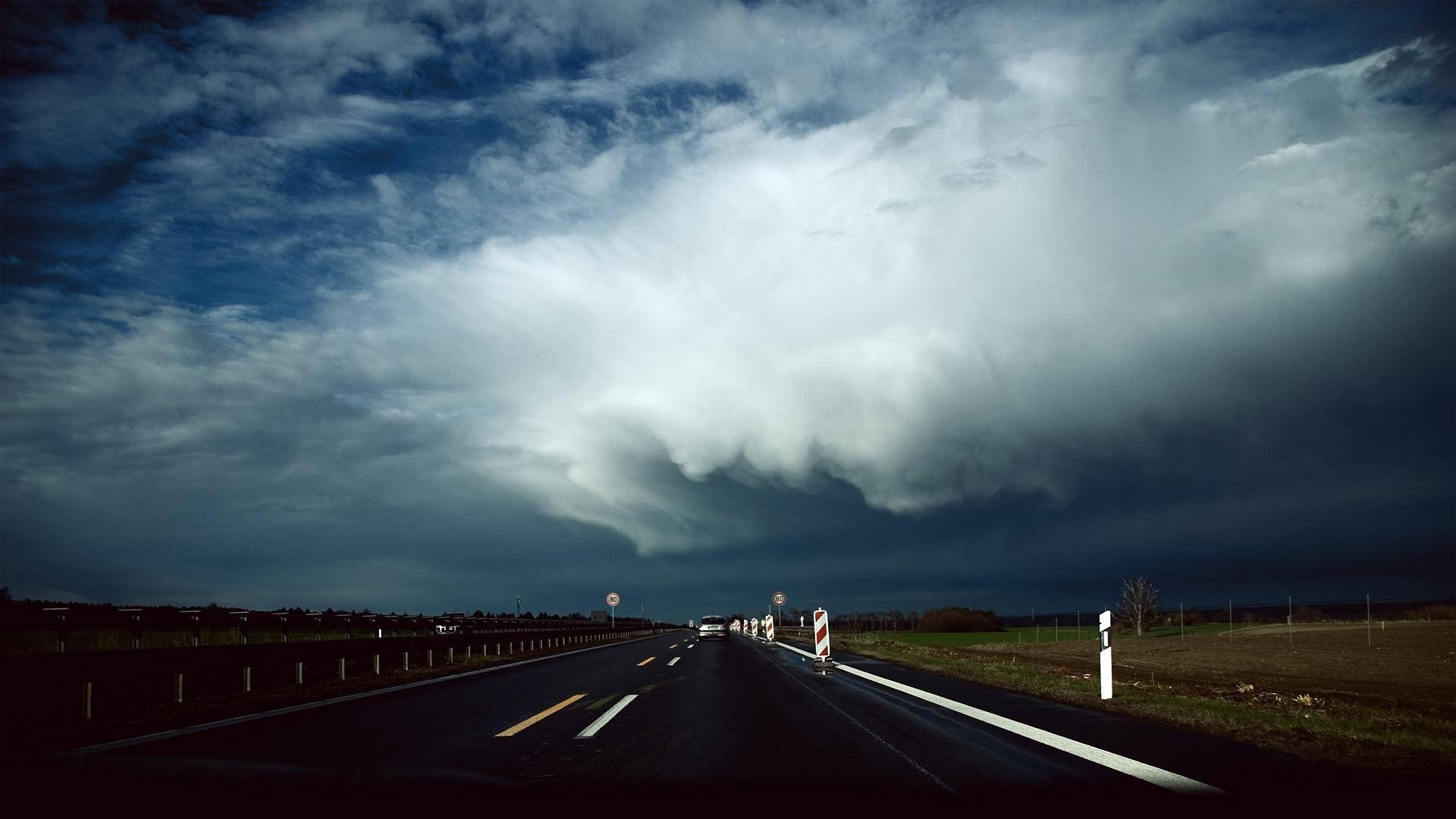 Weather 桌布 壁紙 — 一條孤獨的高速公路伸向在戲劇性的藍天下籠罩著的巨大不祥風暴雲。