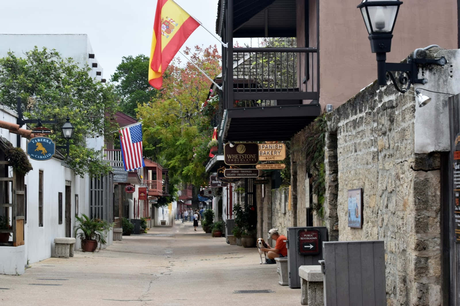 Saint Augustine Florida 桌布 壁紙 — 一條安靜的鵝卵石街道，兩旁是石頭建築和懸掛的旗幟，天空陰沉。
