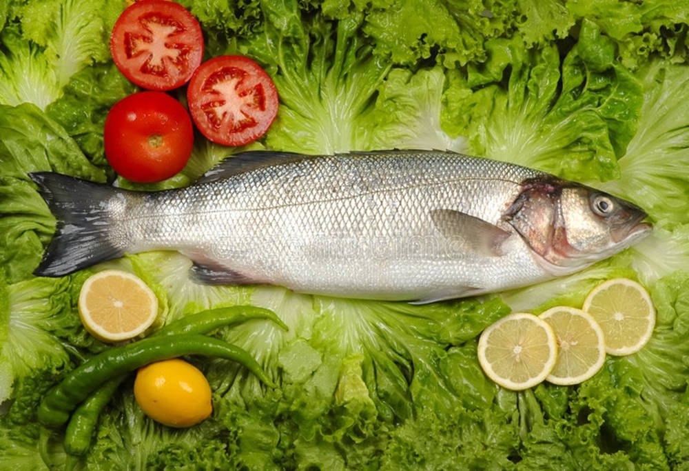 Food Photography 桌布 壁紙 — 一條完整的銀色魚放在脆綠的生菜上，周圍環繞著紅番茄、檸檬片和青辣椒。