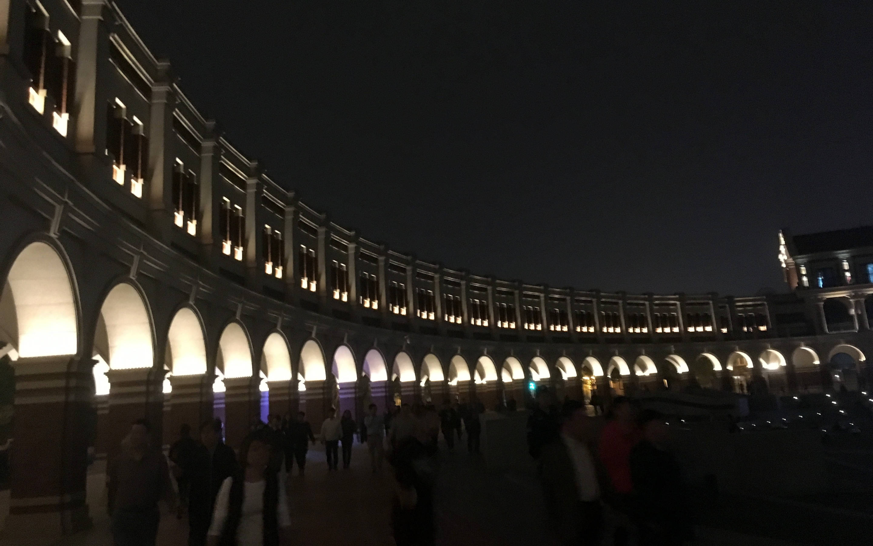 Tianjin 桌布 壁紙 — 一條宏偉的弧形柱廊，發光的拱門照亮了夜晚熙攘的廣場，人們在其溫暖燈光下漫步。