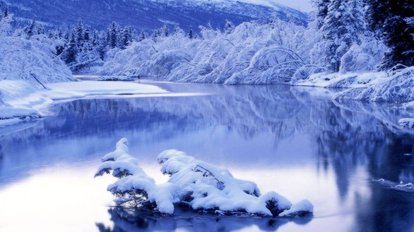 桌布 壁紙 — 一條寧靜的冬日河流，在清涼的藍天下映照著白雪覆蓋的樹木和山脈。