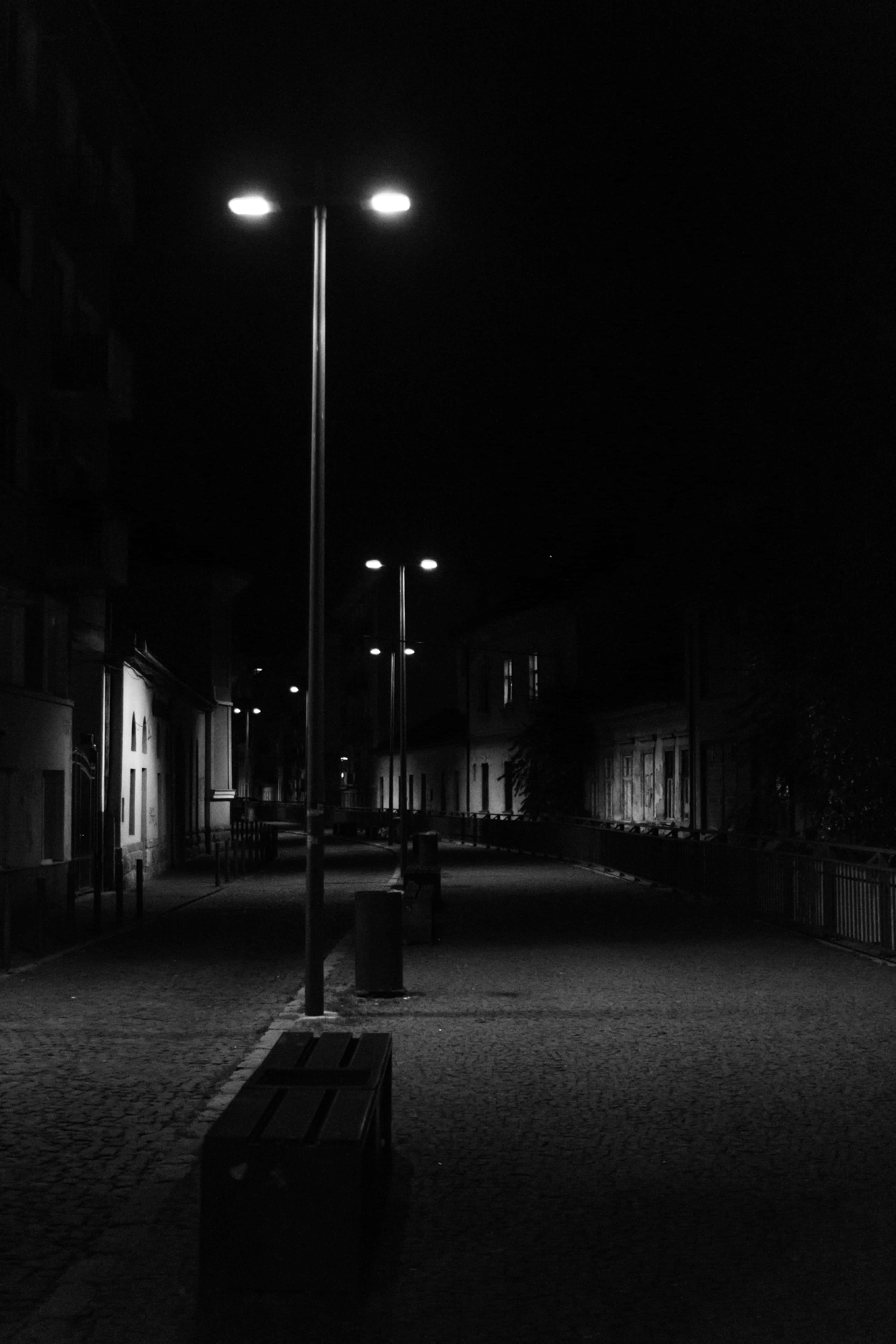 Dark Road 桌布 壁紙 — 一條寧靜的夜晚街道，稀疏的路燈在鵝卵石路面上投下長長的影子。
