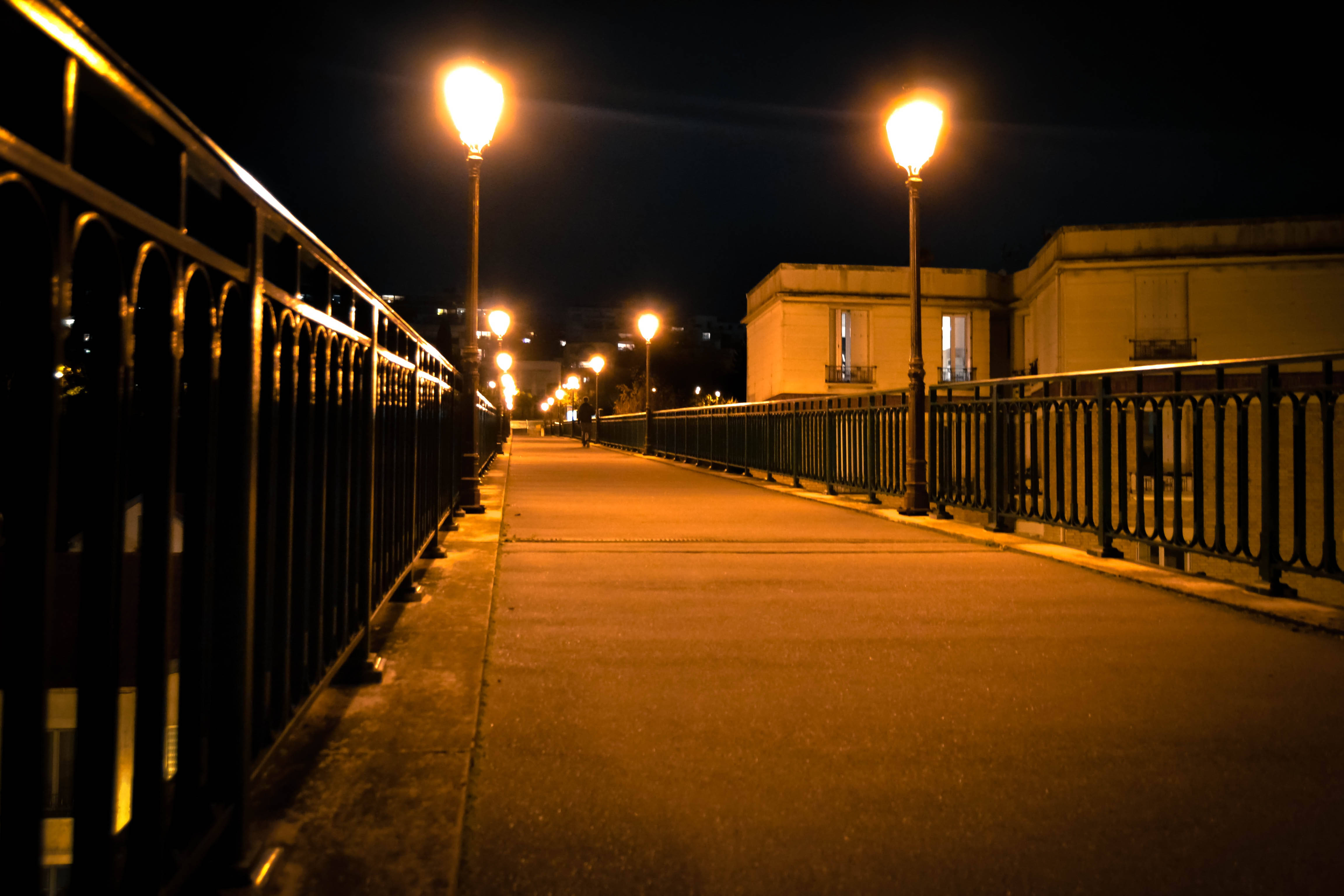Orange City 桌布 壁紙 — 一條寧靜的夜間行人道，由溫暖發光的街燈照亮，在鋪砌的小路上投下長長的影子，兩旁是華麗的欄杆。