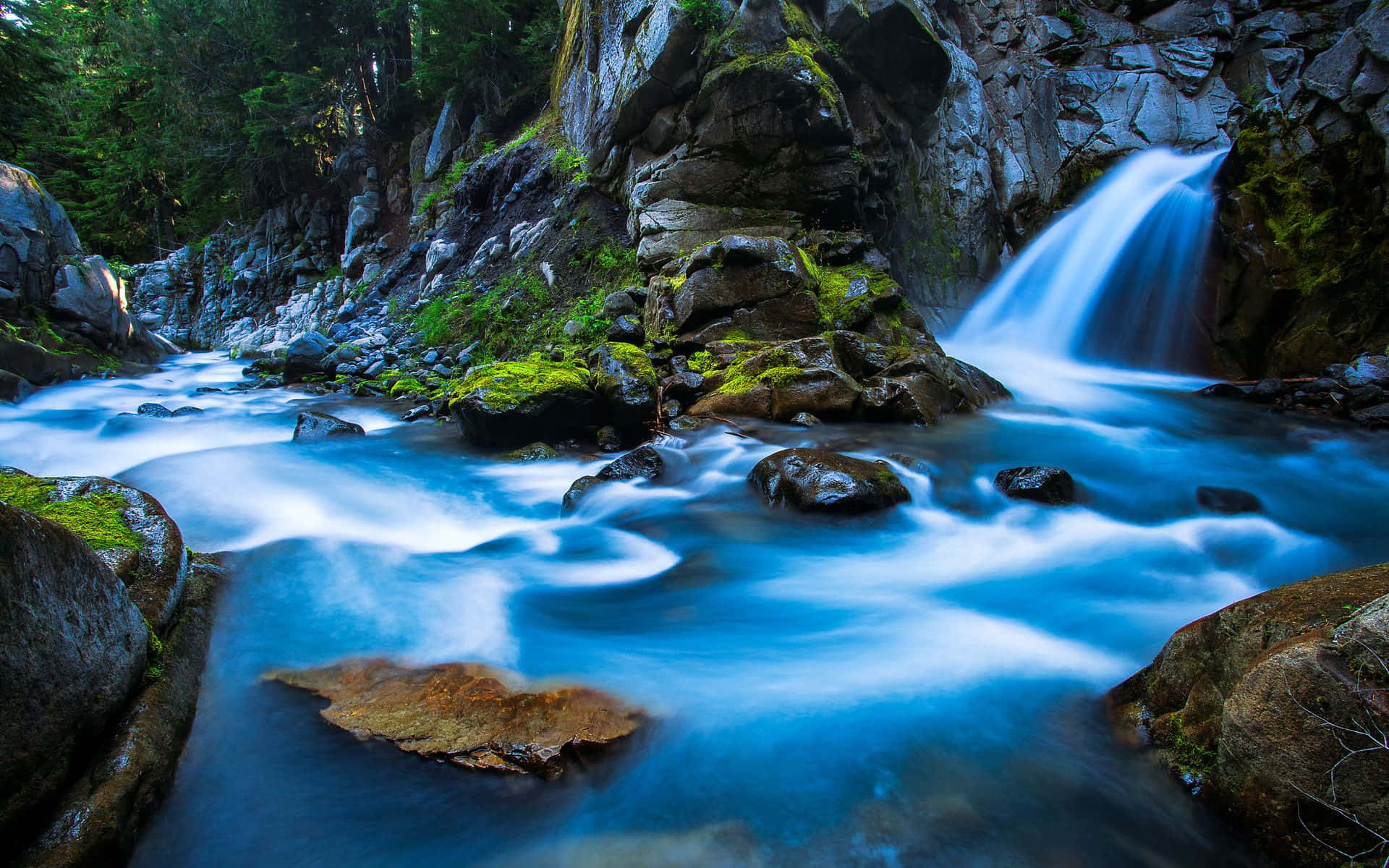 3d Waterfall 桌布 壁紙 — 一條寧靜的山間溪流，帶有藍綠色的水流過長滿青苔的岩石和森林峽谷中的一個小瀑布。