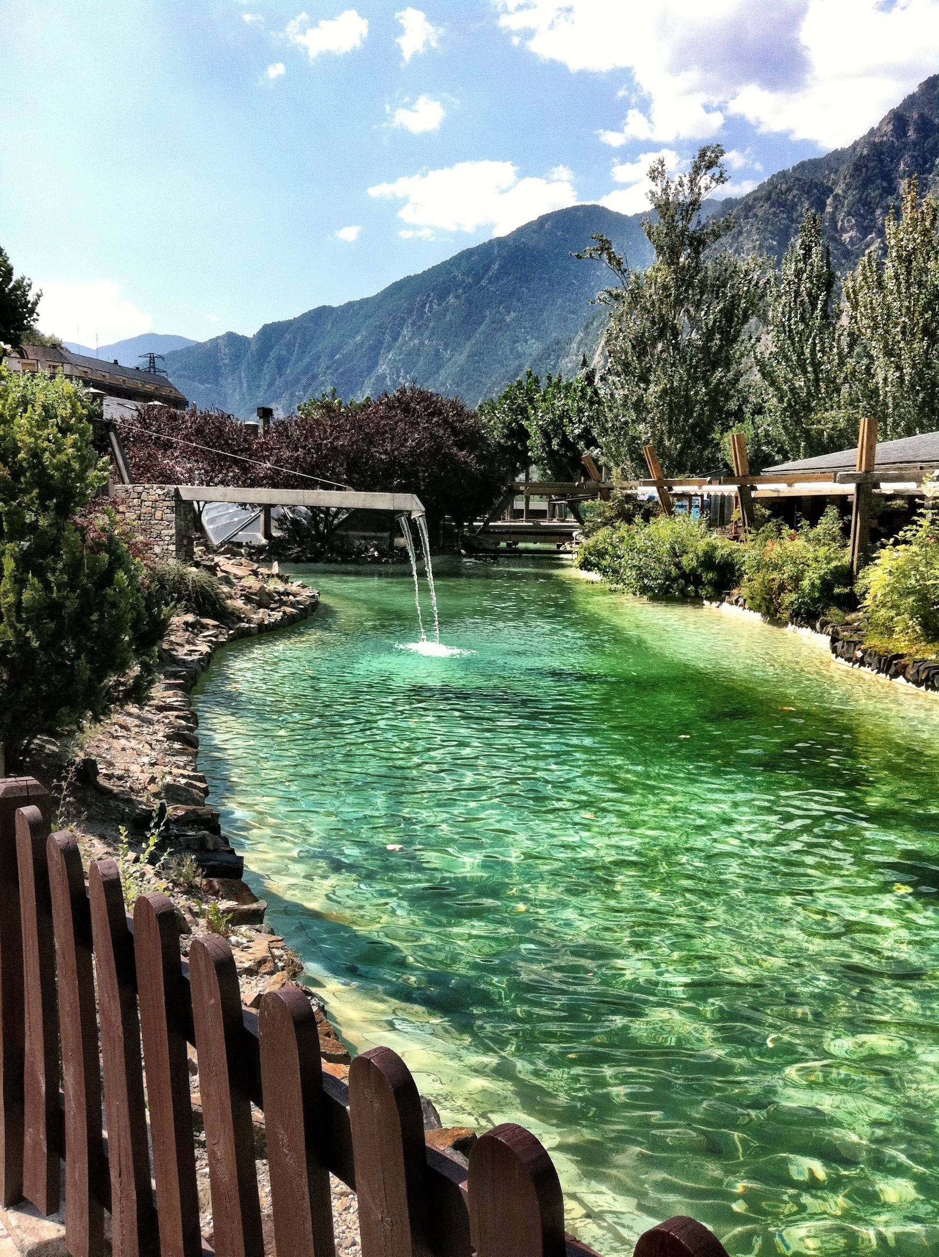 Lake 桌布 壁紙 — 一條寧靜的山間溪流，翠綠色的水流過木柵欄和茂密的植被，在明亮的藍天下。