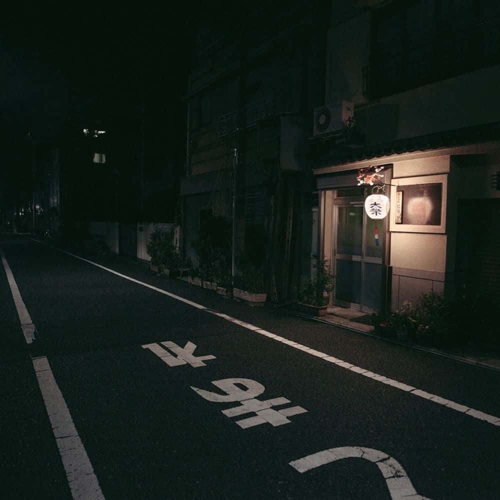 灰色美學動圖 桌布 壁紙 — 一條寧靜的日本街道在夜晚被小商店外一盞發光的燈籠照亮。