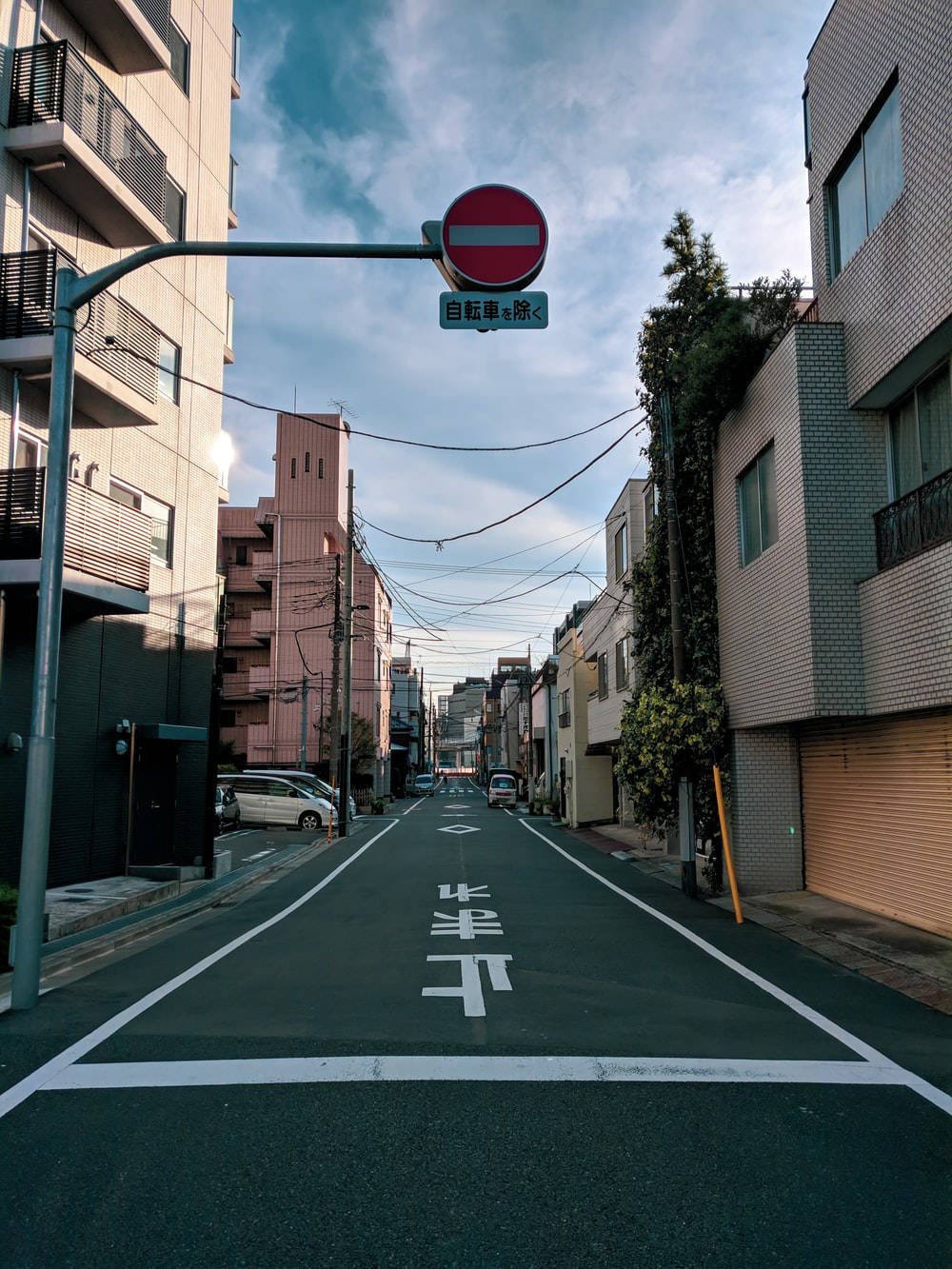 日本 桌布 壁紙 — 一條寧靜的日本街道在部分多雲的天空下延伸至遠方，兩旁有建築物，頭頂有禁止進入標誌。