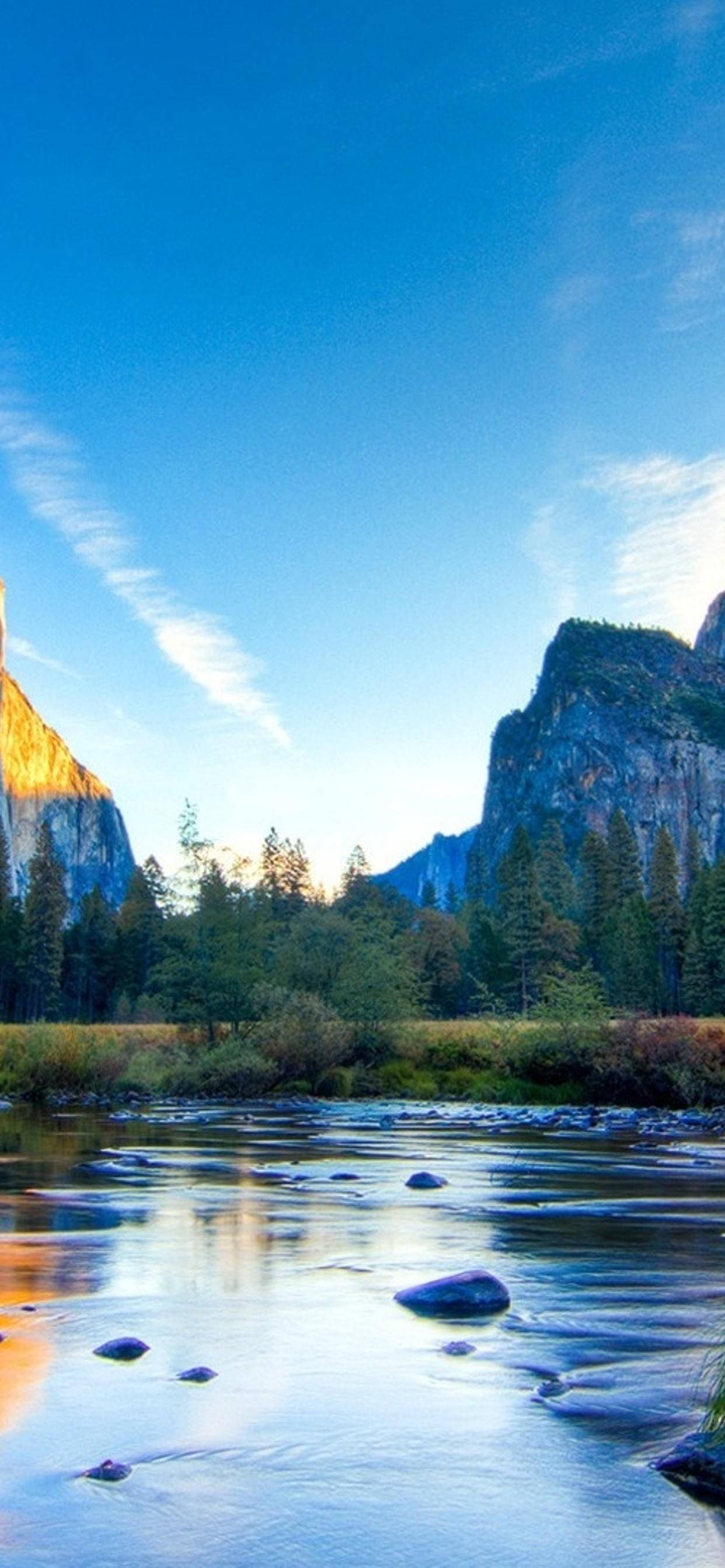 Yosemite iPhone 桌布 壁紙 — 一條寧靜的河流流經兩旁高聳花崗岩懸崖的山谷，上方是清澈藍天，點綴著縷縷白雲。