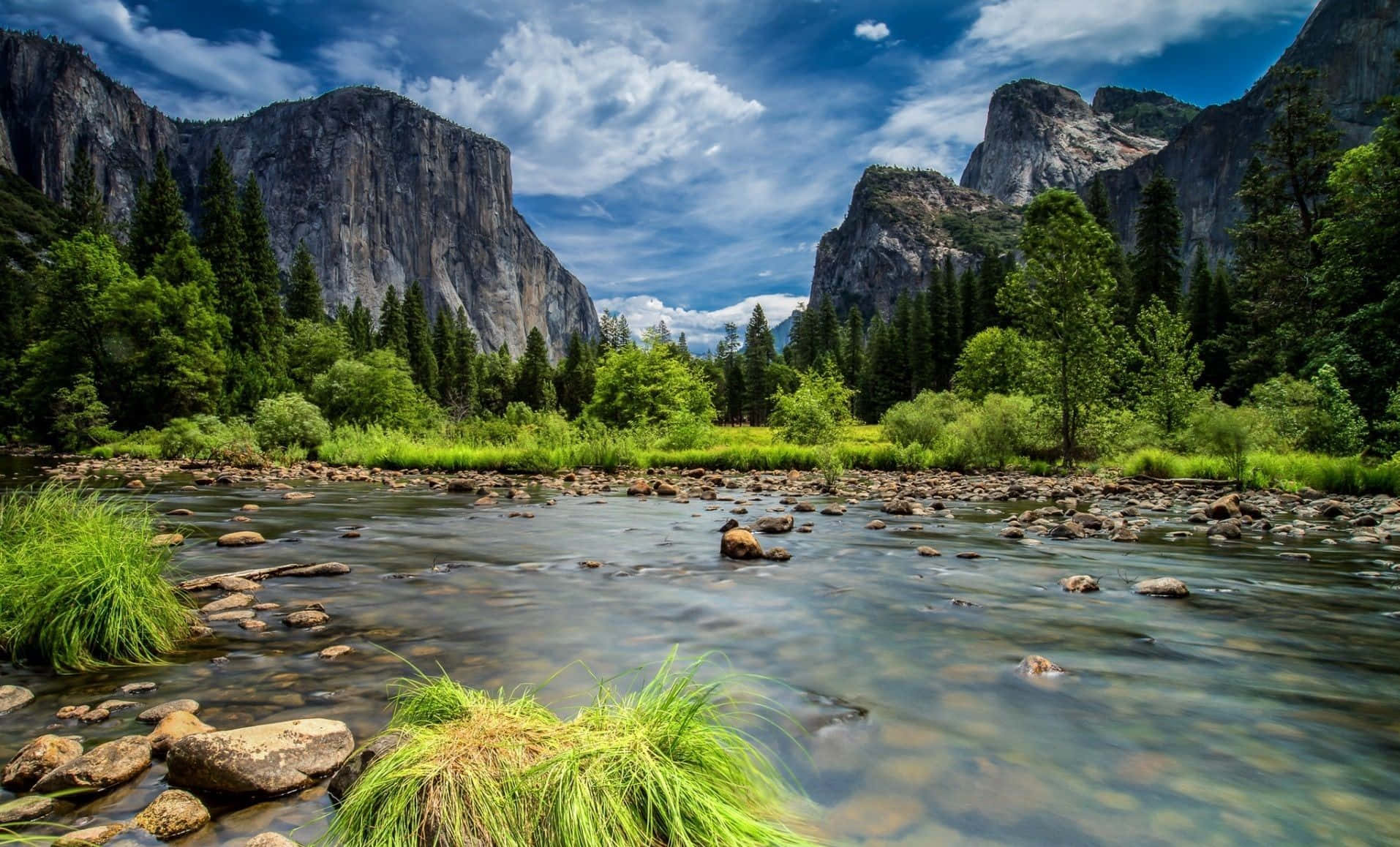 High Sierra 桌布 壁紙 — 一條寧靜的河流流經鬱鬱蔥蔥的綠色山谷，兩旁是高聳的花崗岩懸崖，上方是明亮的藍天和蓬鬆的白雲。
