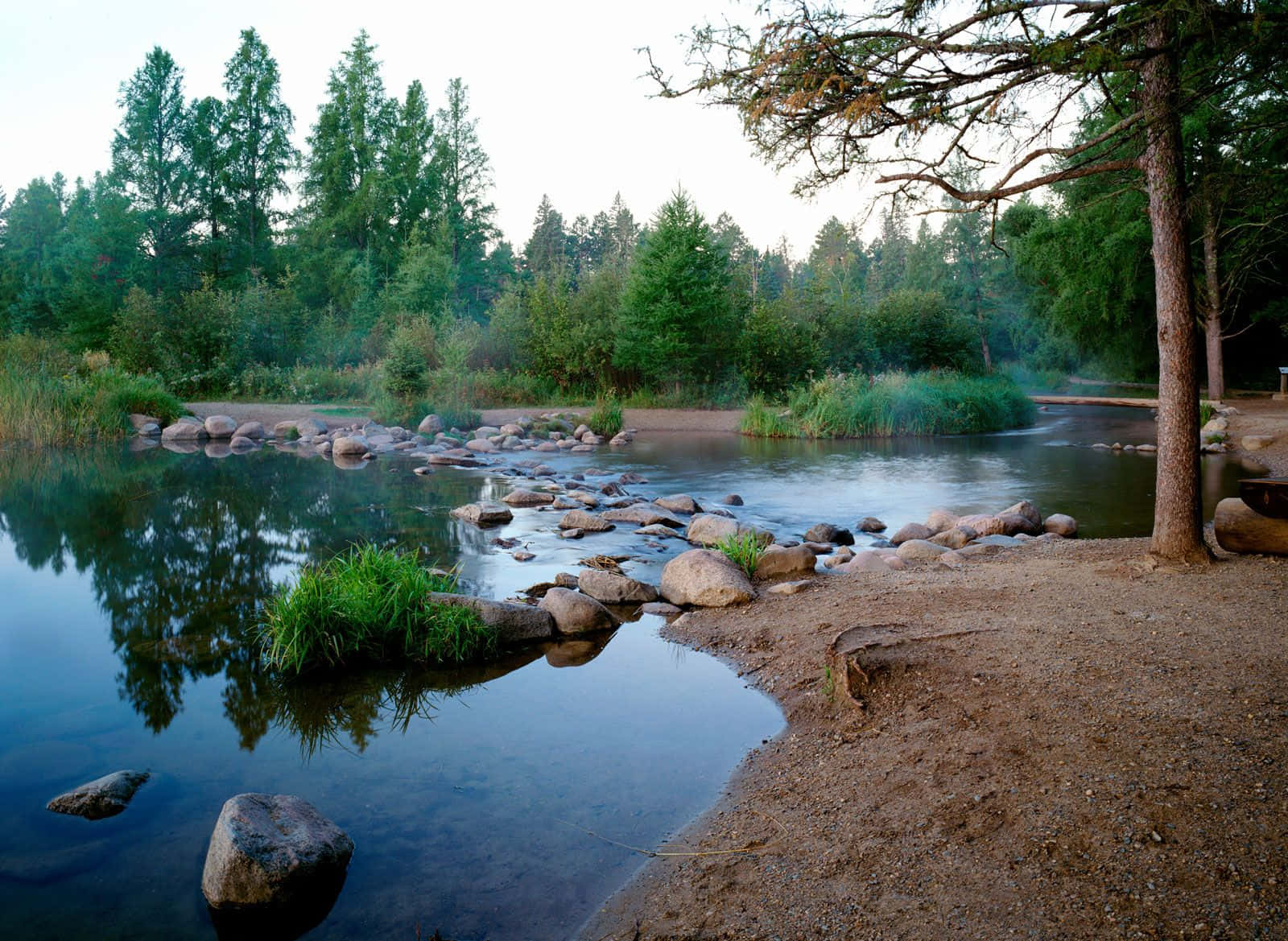 river 桌布 壁紙 — 一條寧靜的河流蜿蜒穿過森林地區，岩石和樹木在黎明時分倒映在平靜的水面上。