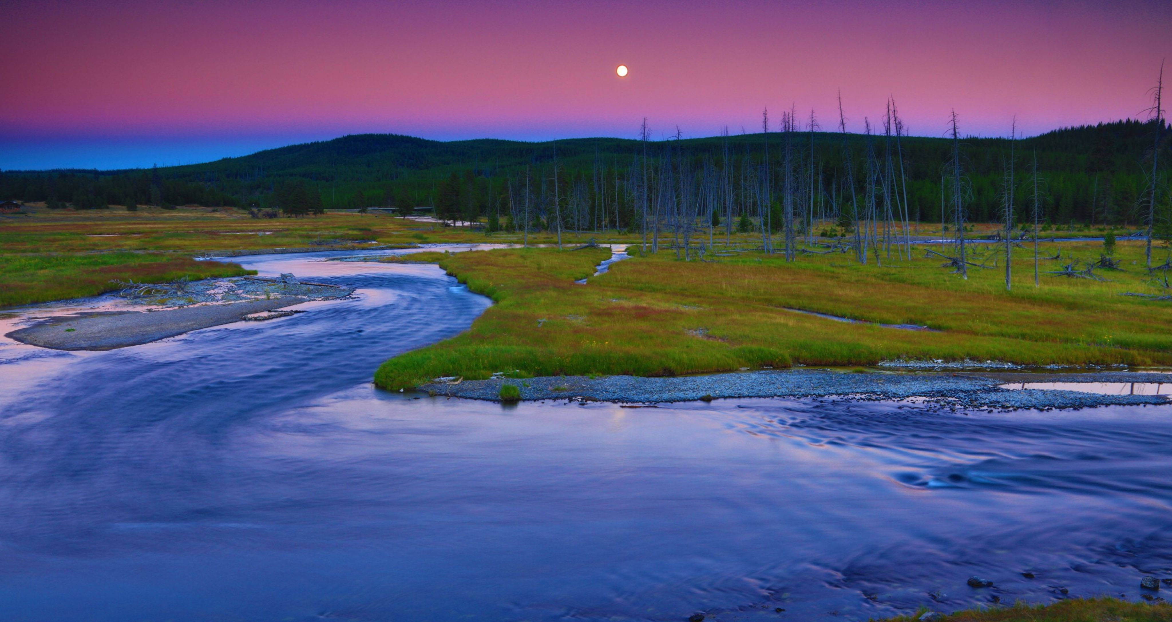 Yellowstone 桌布 壁紙 — 一條寧靜的河流蜿蜒穿過草地平原，在充滿活力的粉紅色和紫色暮色天空下，伴隨著一輪發光的月亮。