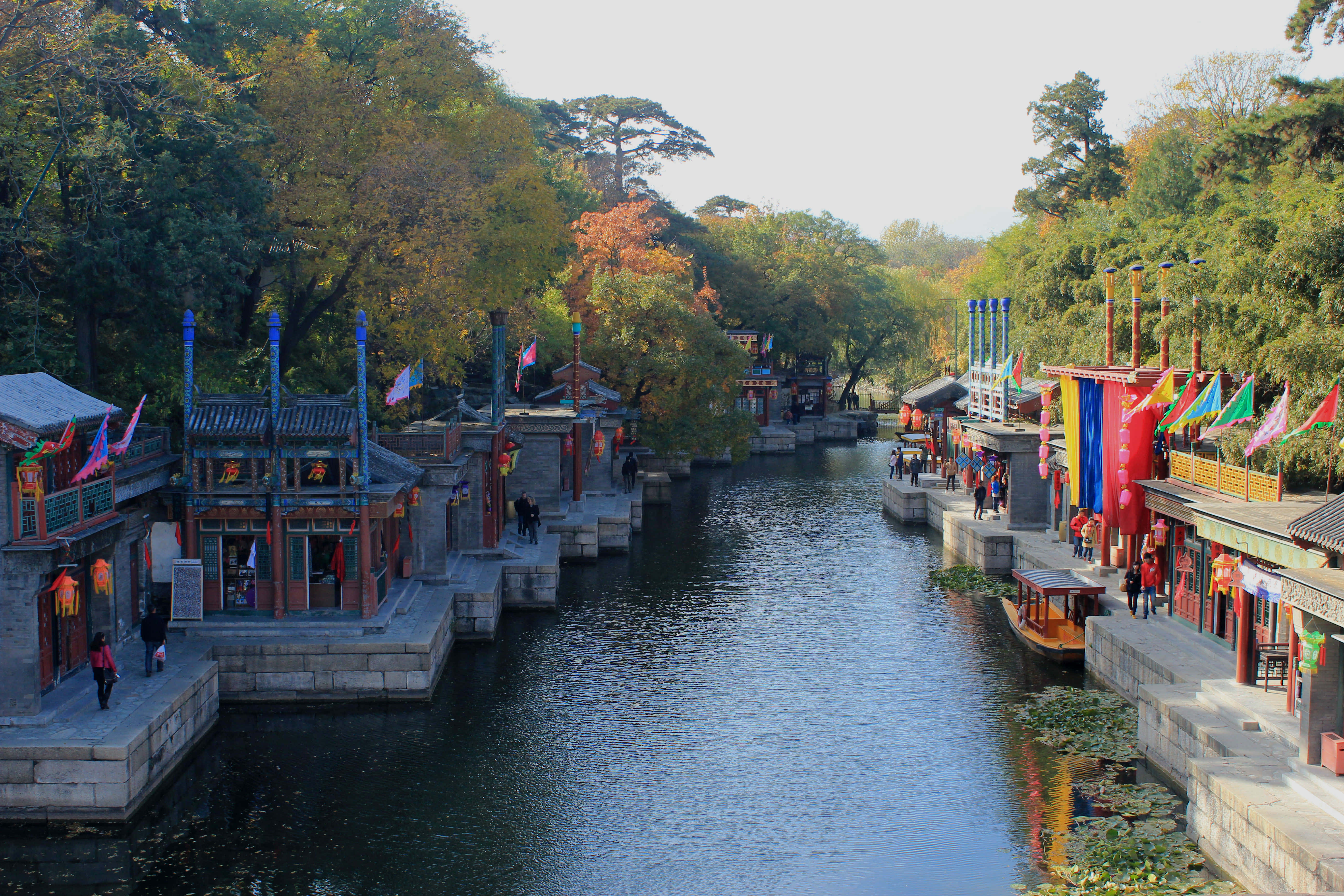 Lake 桌布 壁紙 — 一條寧靜的運河蜿蜒穿過傳統中式建築，兩旁有秋樹和彩色旗幟點綴水道。