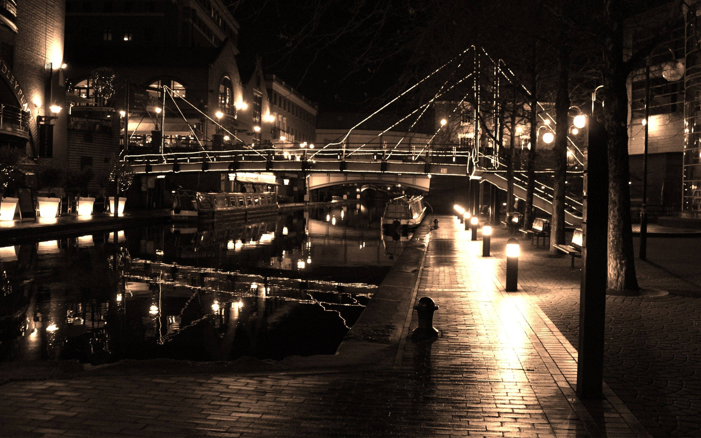 Birmingham 桌布 壁紙 — 一條寧靜運河的棕褐色夜景，有一座亮燈的行人橋和發光的燈光倒映在水中。
