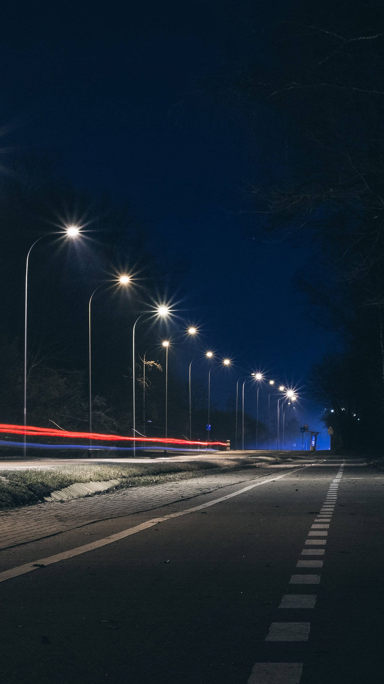 Smartphone 桌布 壁紙 — 一條寧靜道路的長時間曝光夜景，兩旁有發光的街燈和紅色車燈的條紋。