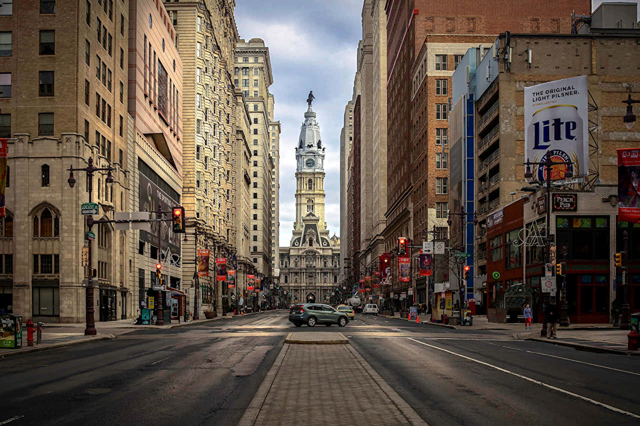 Philly 桌布 壁紙 — 一條寬闊的城市街道兩旁高樓林立，通向陰雲天空下高聳的鐘樓。