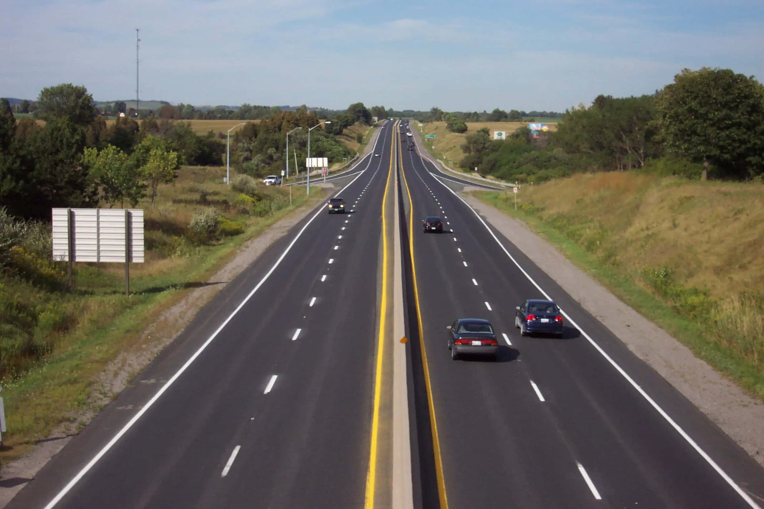 highway 桌布 壁紙 — 一條寬闊的高速公路在晴朗的藍天下延伸至遠方，兩邊都有汽車行駛。