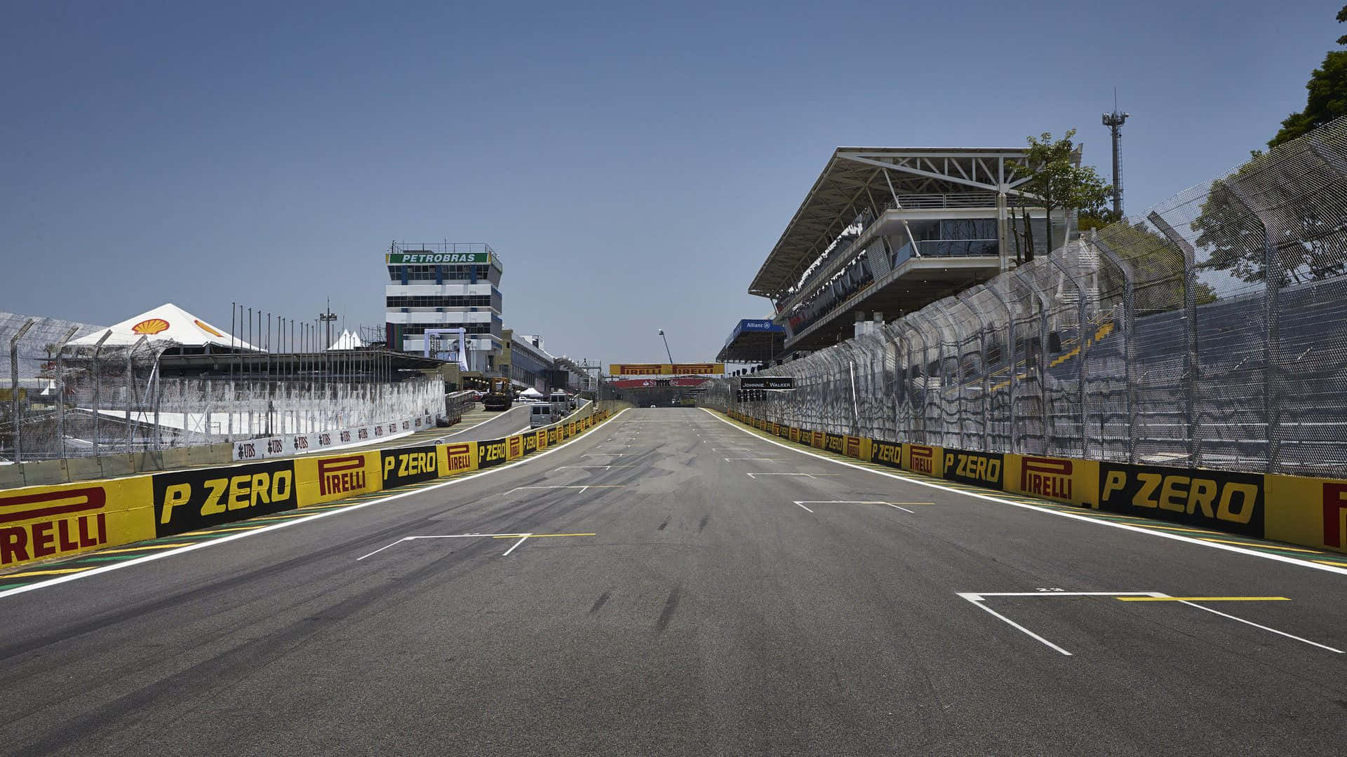 Race Track 桌布 壁紙 — 一條寬闊空蕩的賽道在晴朗藍天下延伸至看台，瀝青路面上有 Pirelli 品牌標誌。
