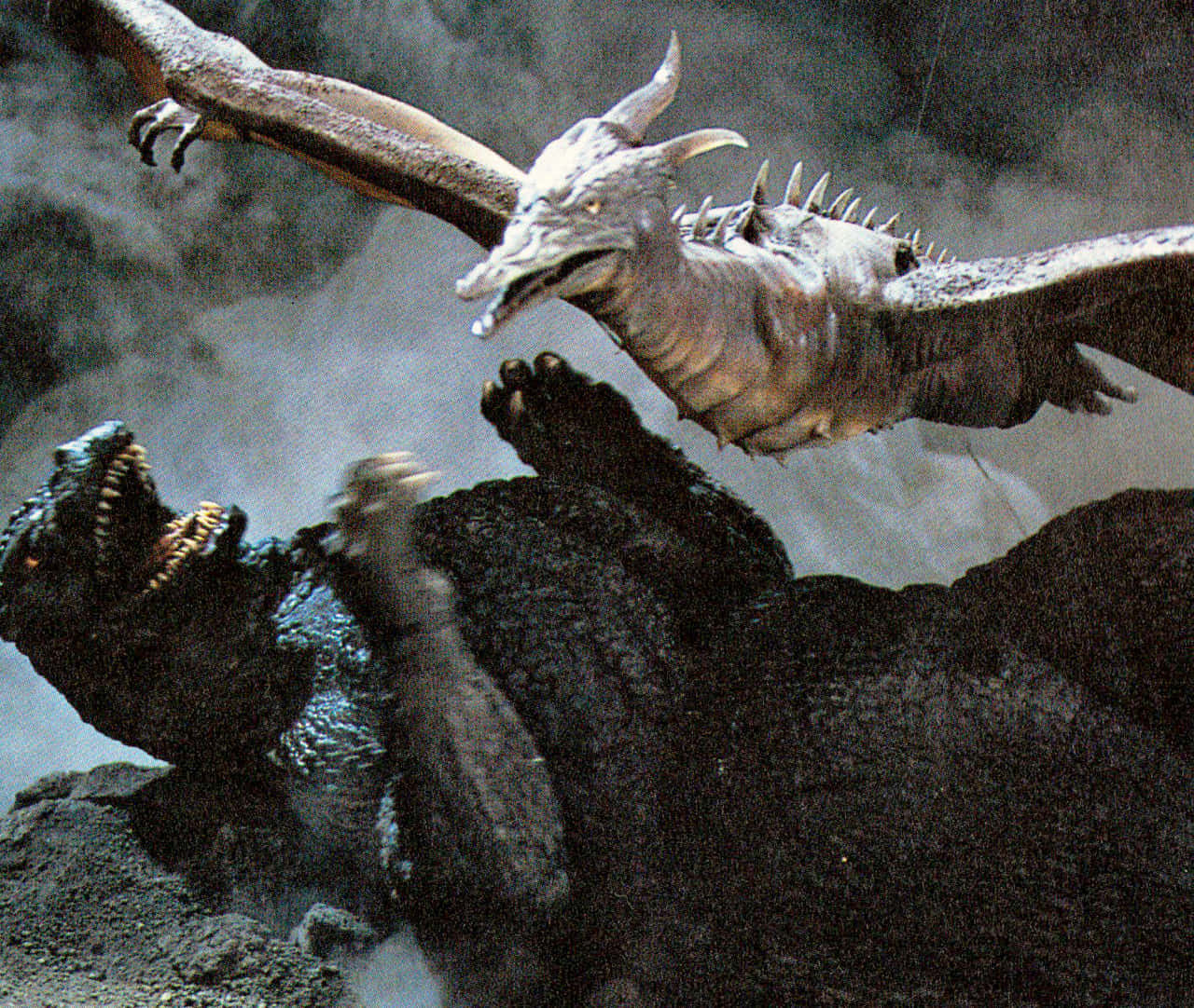 Godzilla Vs Rodan 桌布 壁紙 — 一條巨龍在咆哮的哥吉拉上方翱翔，四周煙霧繚繞，火山岩遍布。
