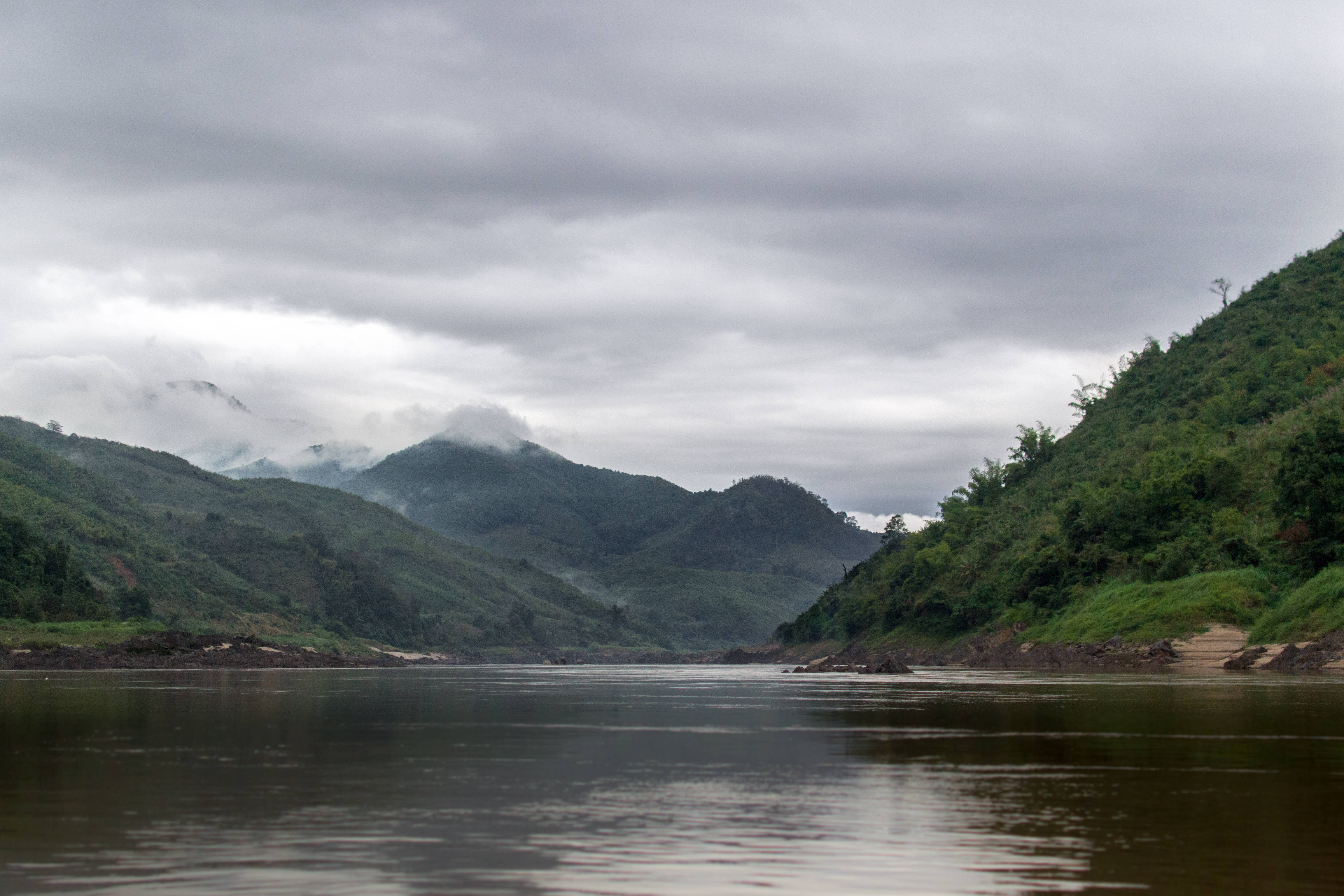 Laos 桌布 壁紙 — 一條平靜的河流蜿蜒穿過鬱鬱蔥蔥的青山，天空陰沉，薄霧籠罩著遠峰。