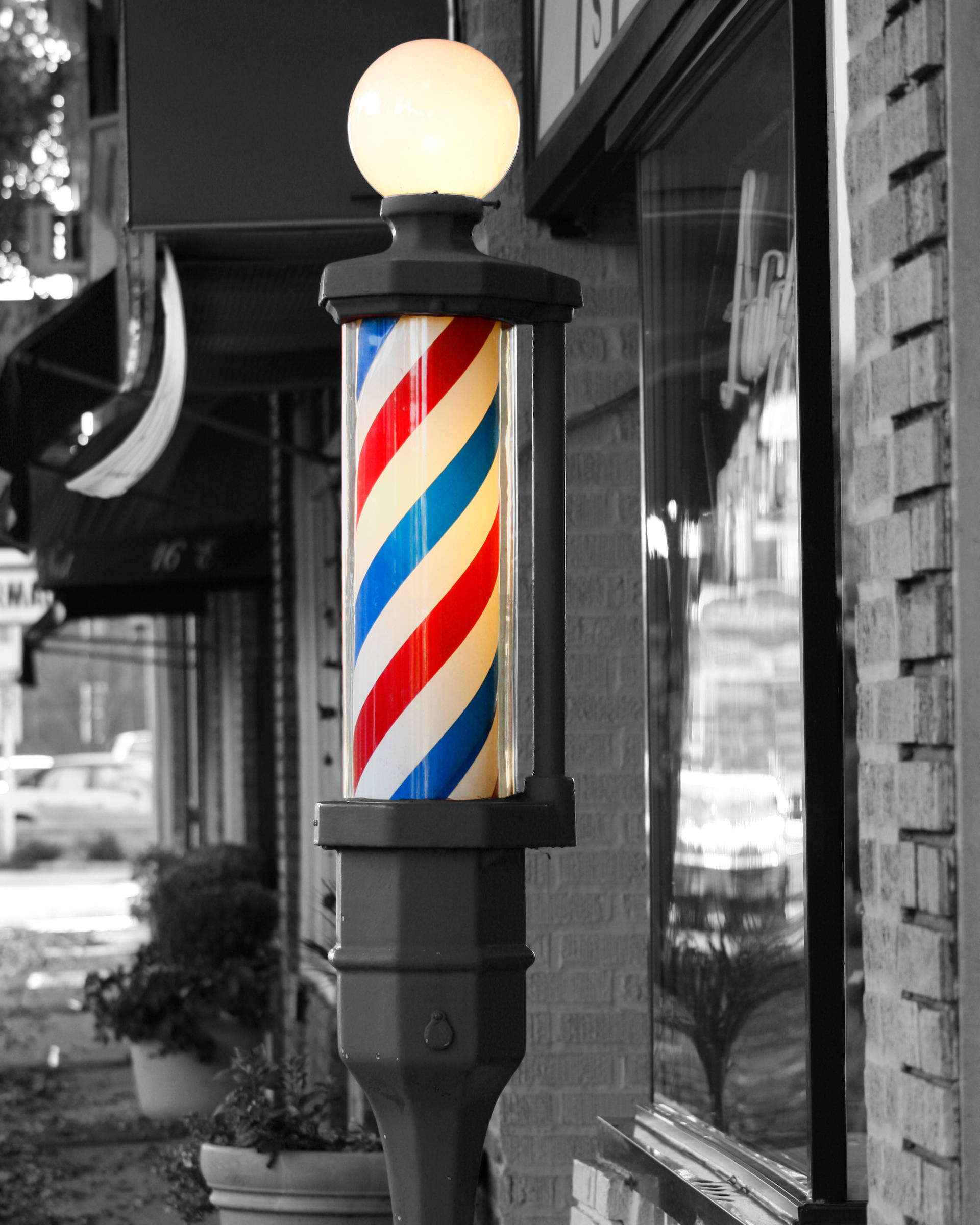 Barber 桌布 壁紙 — 一條復代理髮店旋轉燈柱，帶有紅、白、藍斜條紋，在黑白城市街景中溫暖地發光。