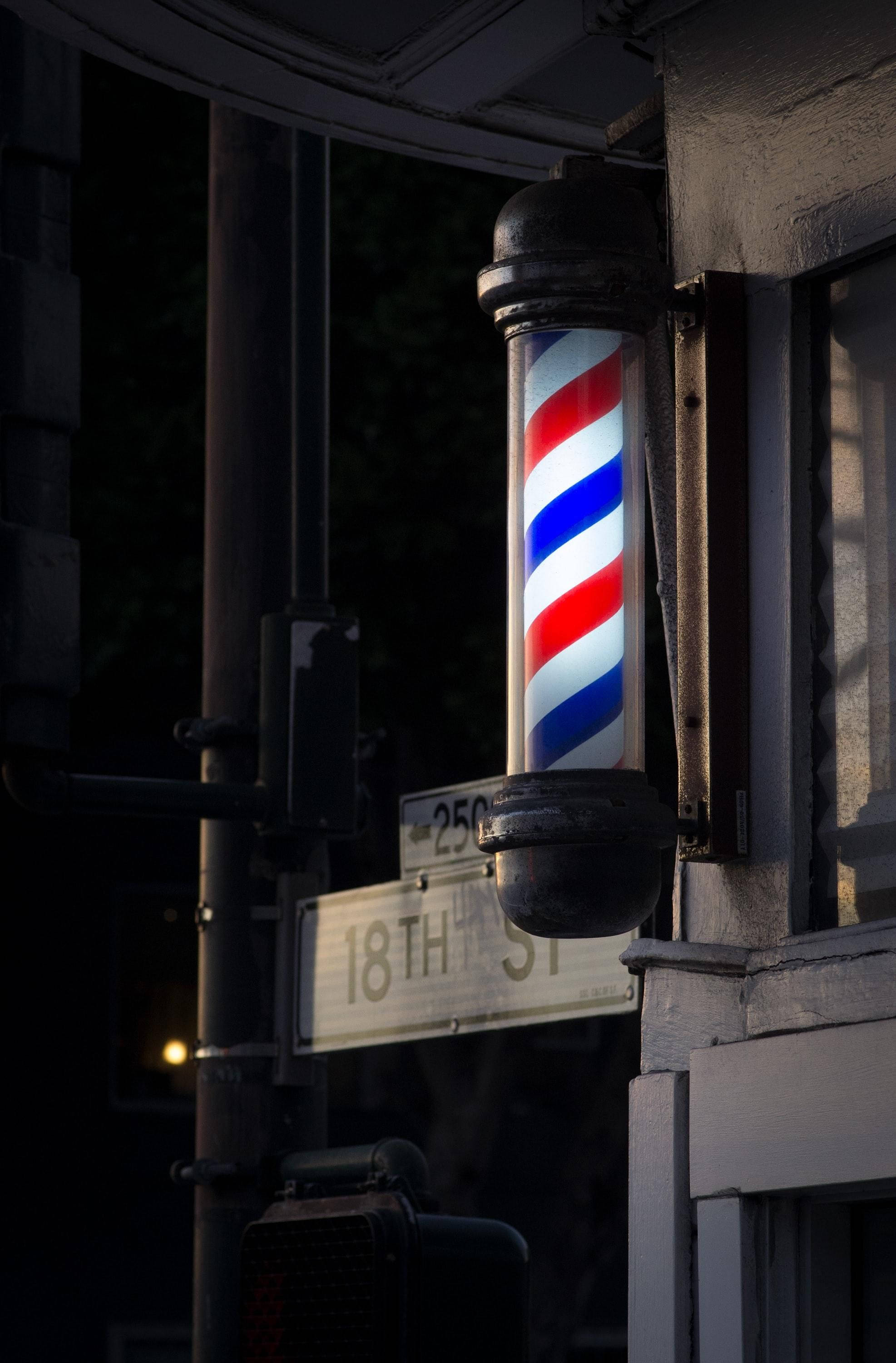 Barber 桌布 壁紙 — 一條復代理髮柱，帶有紅、白、藍條紋，在夜晚昏暗的城市街道上溫暖地發光。