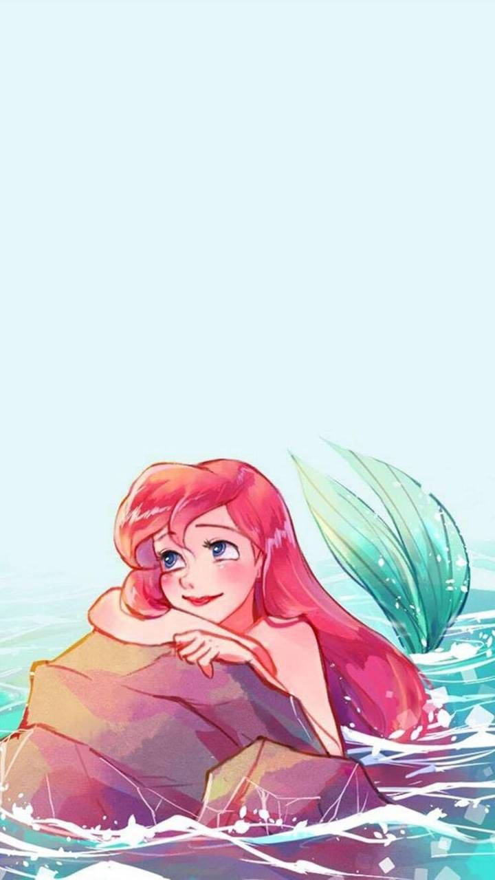 愛麗兒 桌布 壁紙 — 一條快樂的長紅髮綠尾美人魚在清澈的碧綠水中，在柔和的藍天下，在岩石上休息。